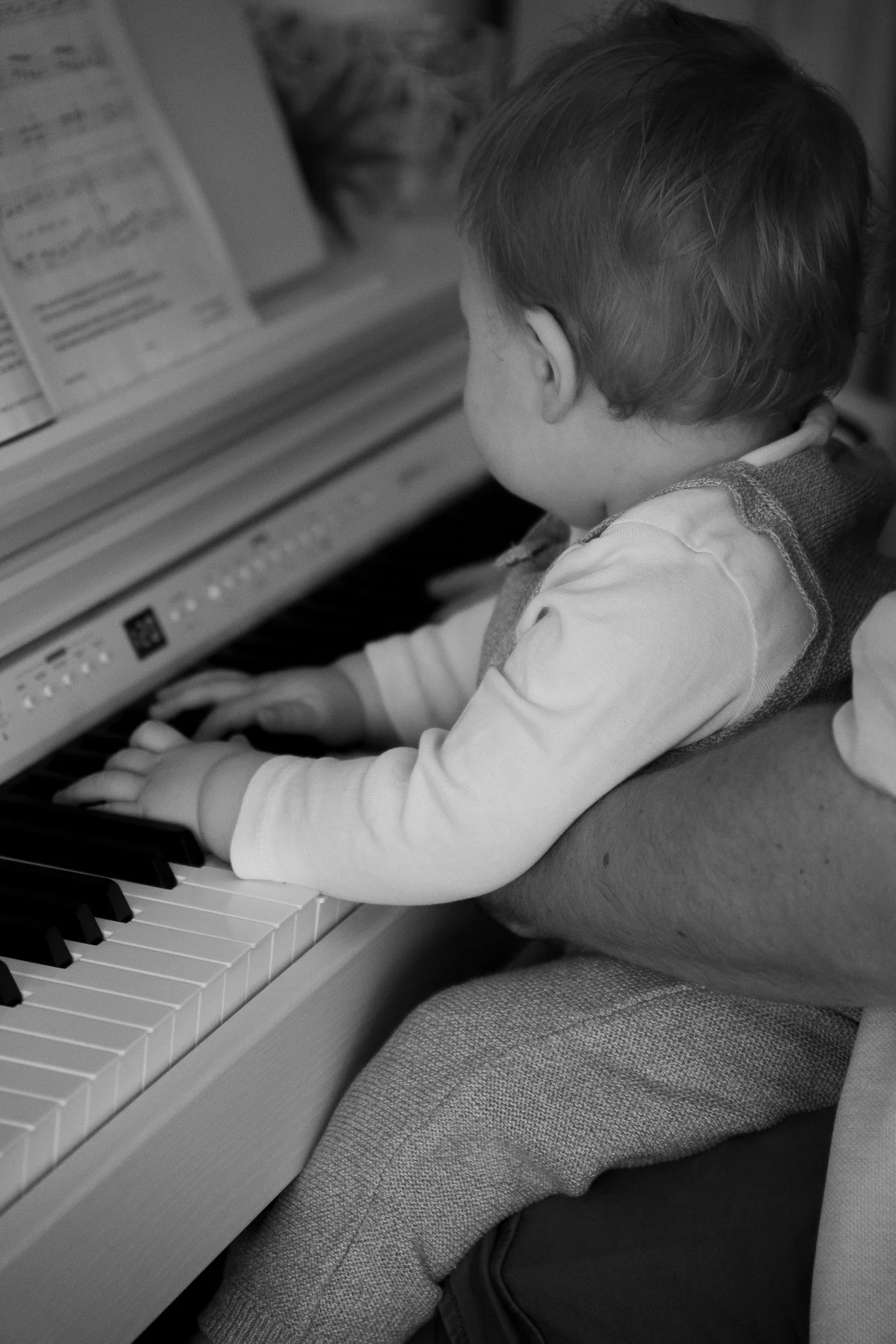 Ein kleiner Junge spielt Klavier, auf dem Schoß eines Erwachsenen.