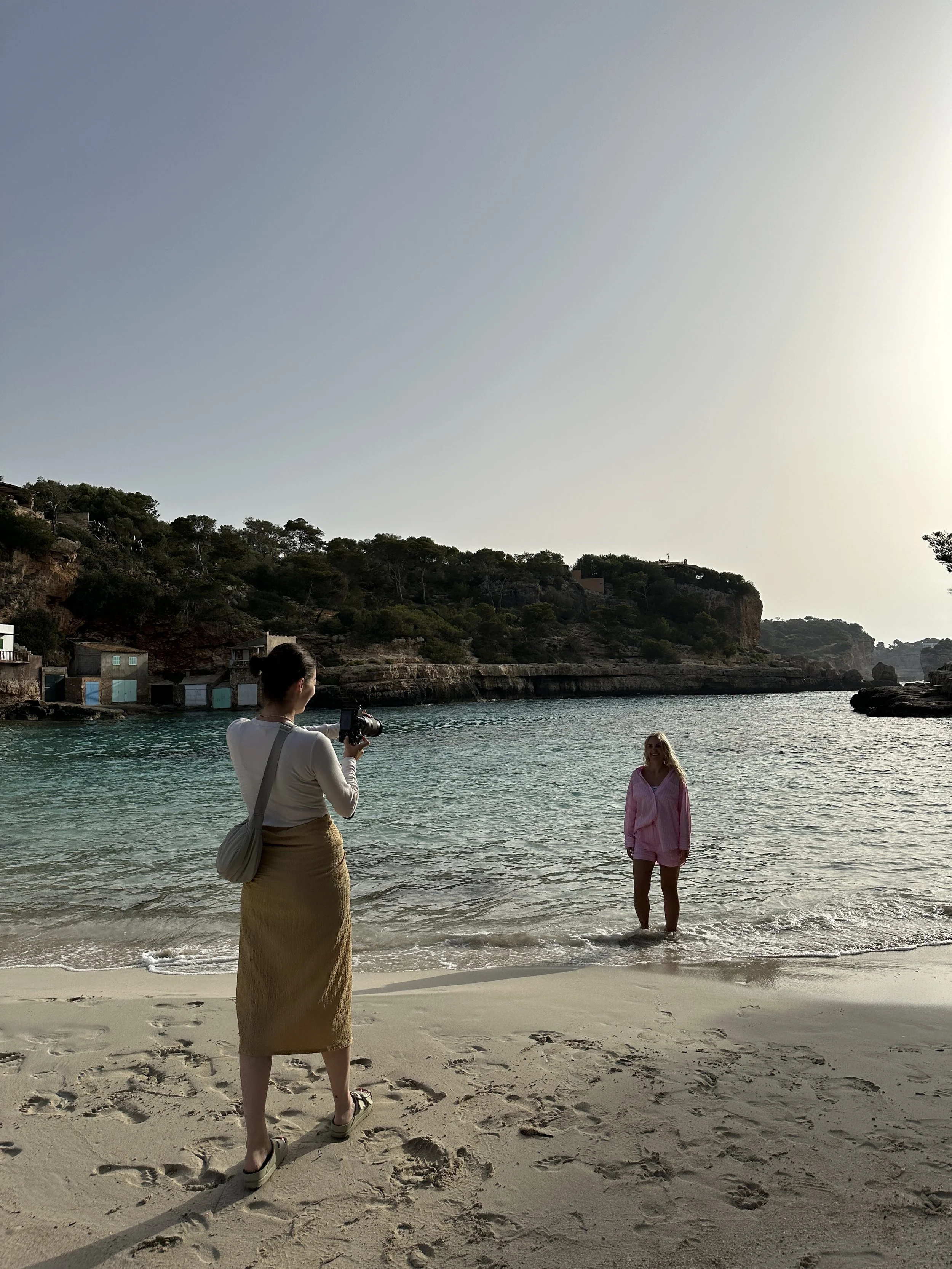Eine Frau macht ein Foto von einer anderen Frau, die im Wasser an einem Strand steht.