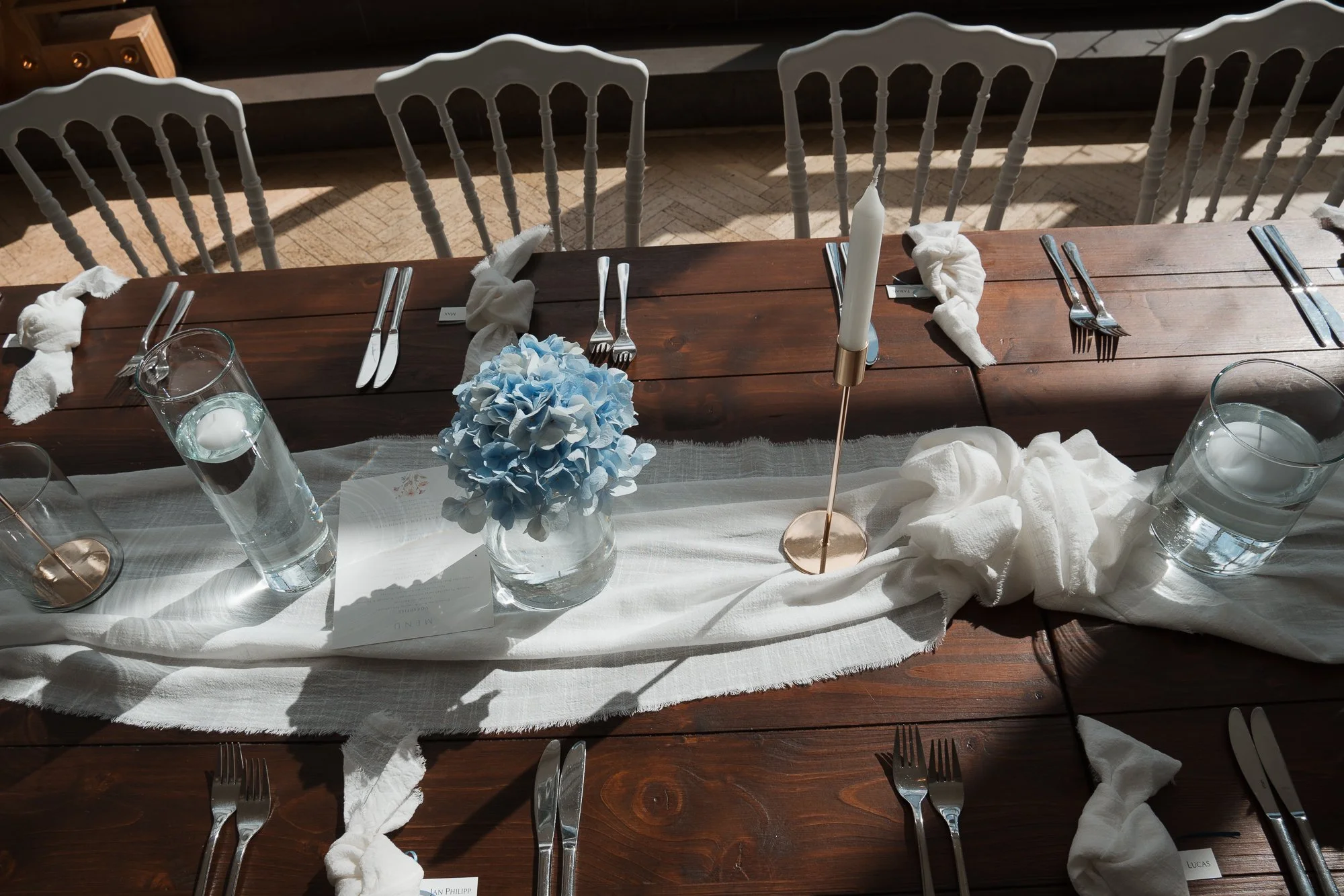 Elegant gedeckter Tisch mit weißen Tüchern, Kerzen, einem blauen Hortensienstrauß und Besteck, bereit für eine Feier oder ein Fest