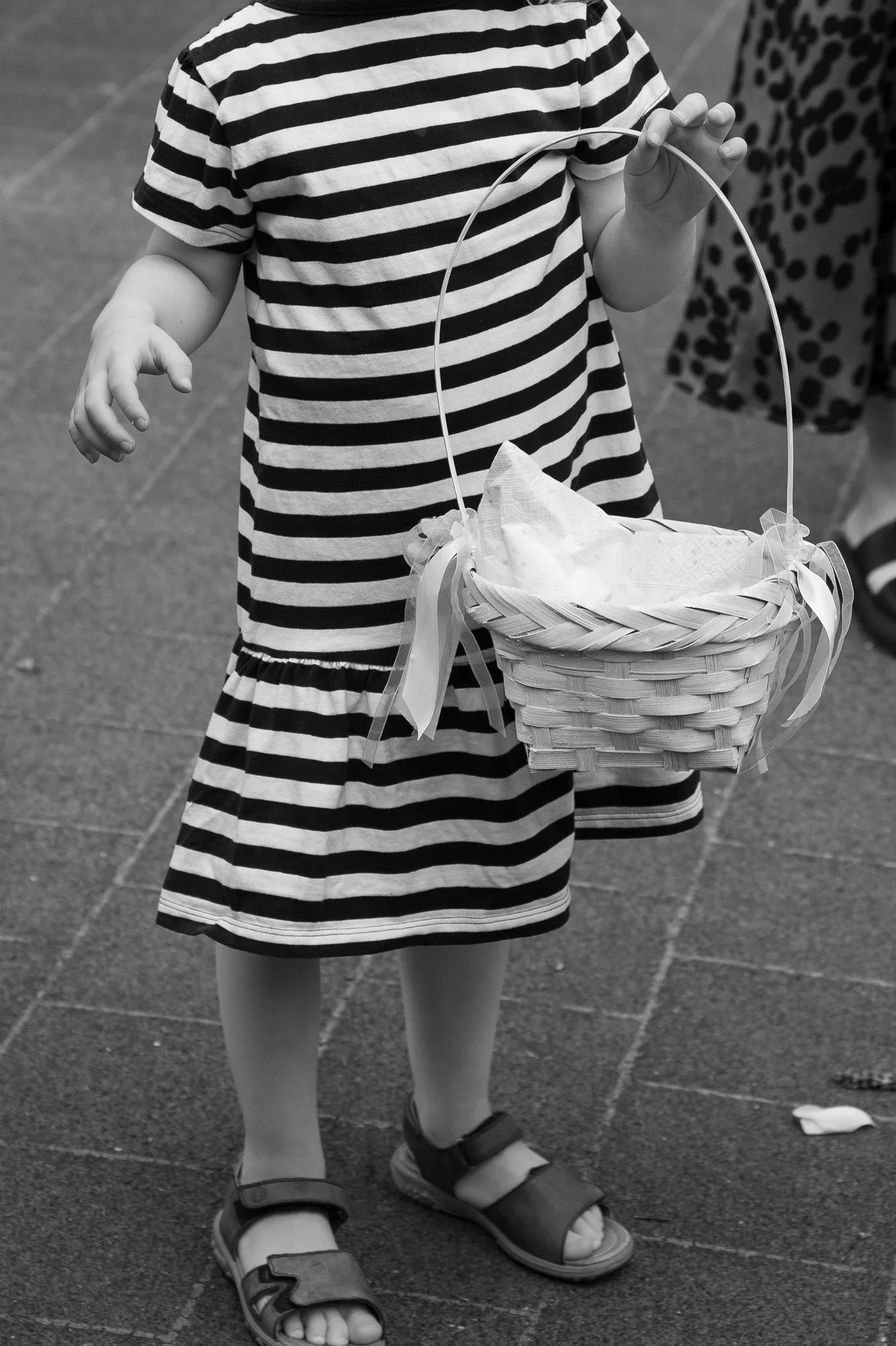 Ein kleines Mädchen in einem gestreiften Kleid mit Sandalen hält einen Korb mit Geschenkpapier darin.