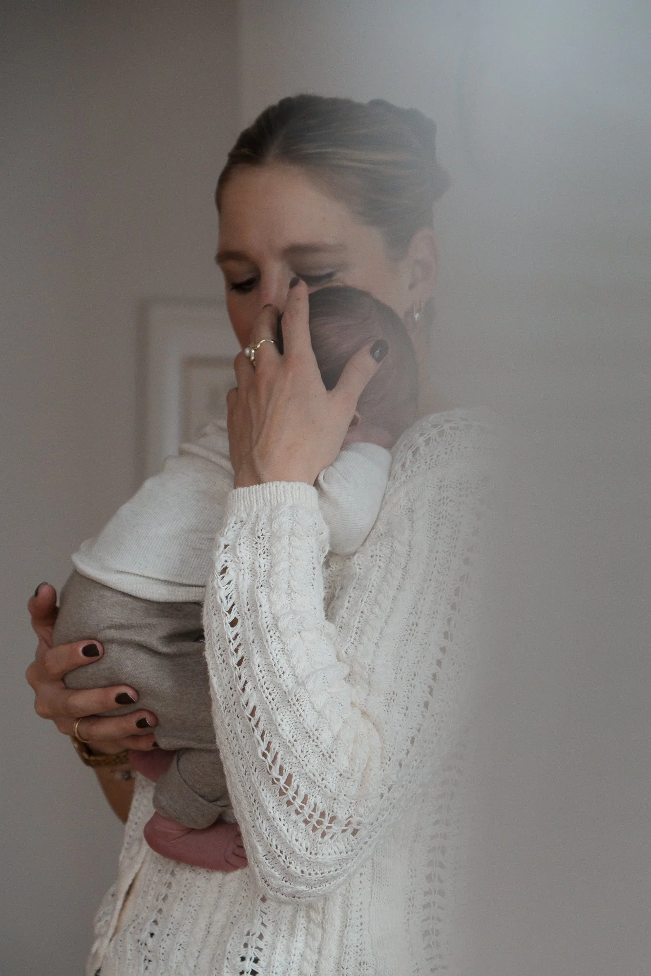 Eine Frau umarmt ein Baby, beide scheinen tröstend und liebevoll verbunden, die Frau trägt einen weißen, netzartigen Pullover.