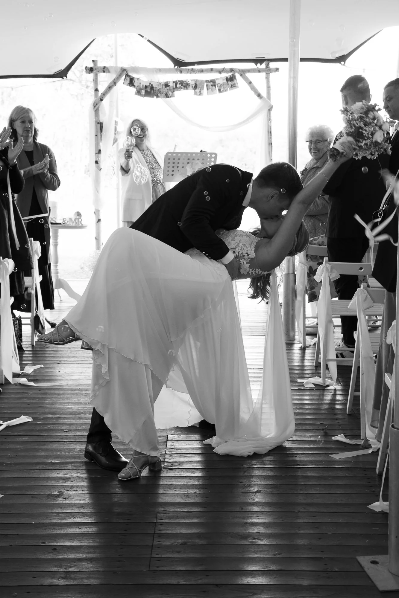 Braut und Bräutigam tanzen bei ihrer Hochzeit, umgeben von Gästen in einem festlich dekorierten Zelt.