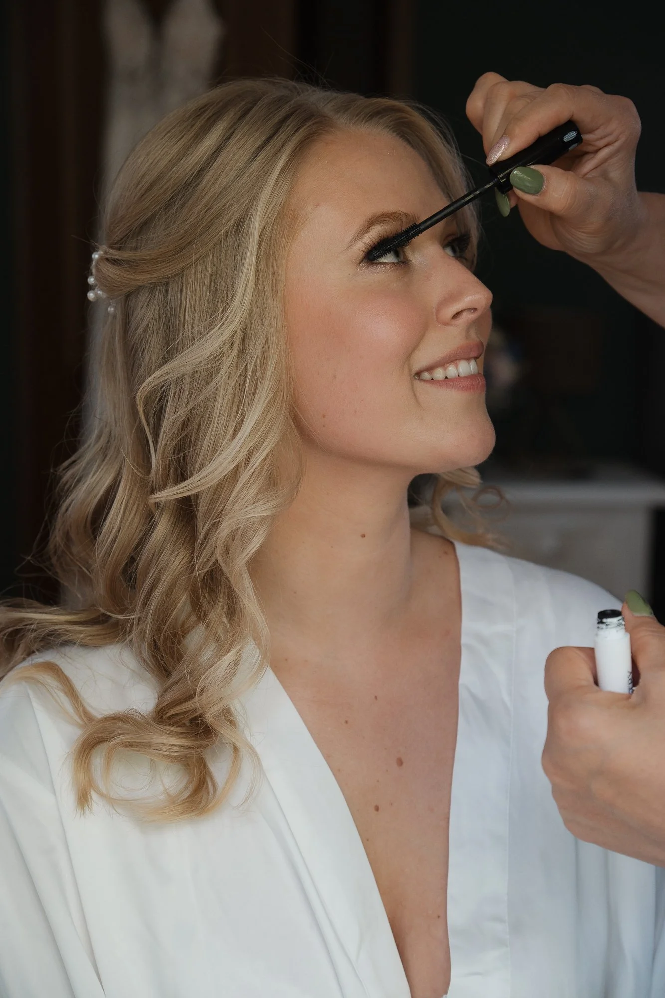 Eine Frau erhält Make-up, der Kosmetikerin trägt grünen Nagellack und verwendet Mascara auf die Wimpern der Frau.