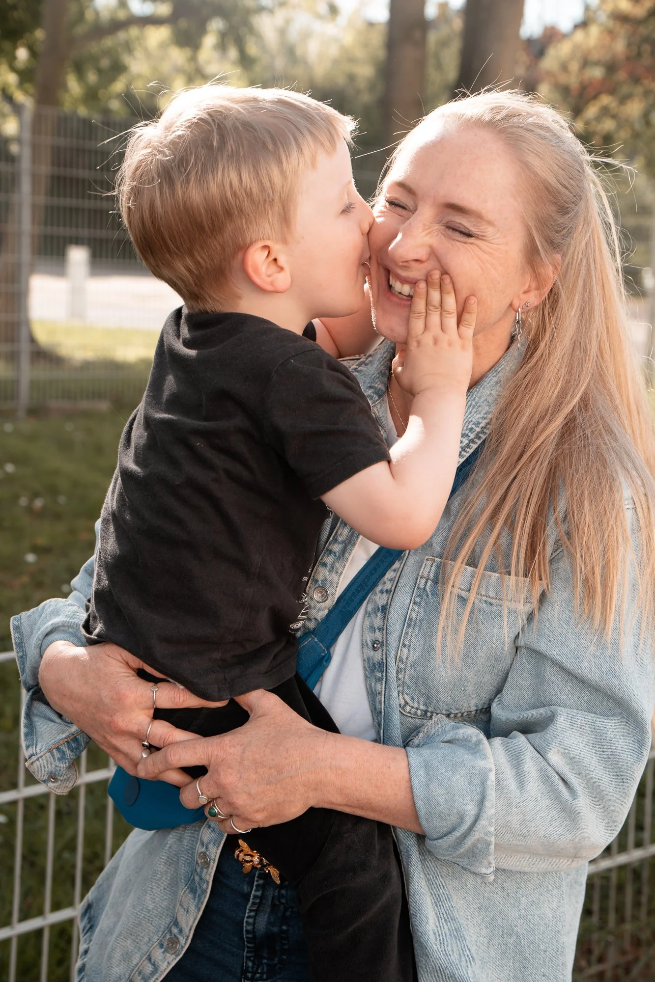 Ein Junge küsst seine lachende Mutter im Freien, während sie sich umarmen.