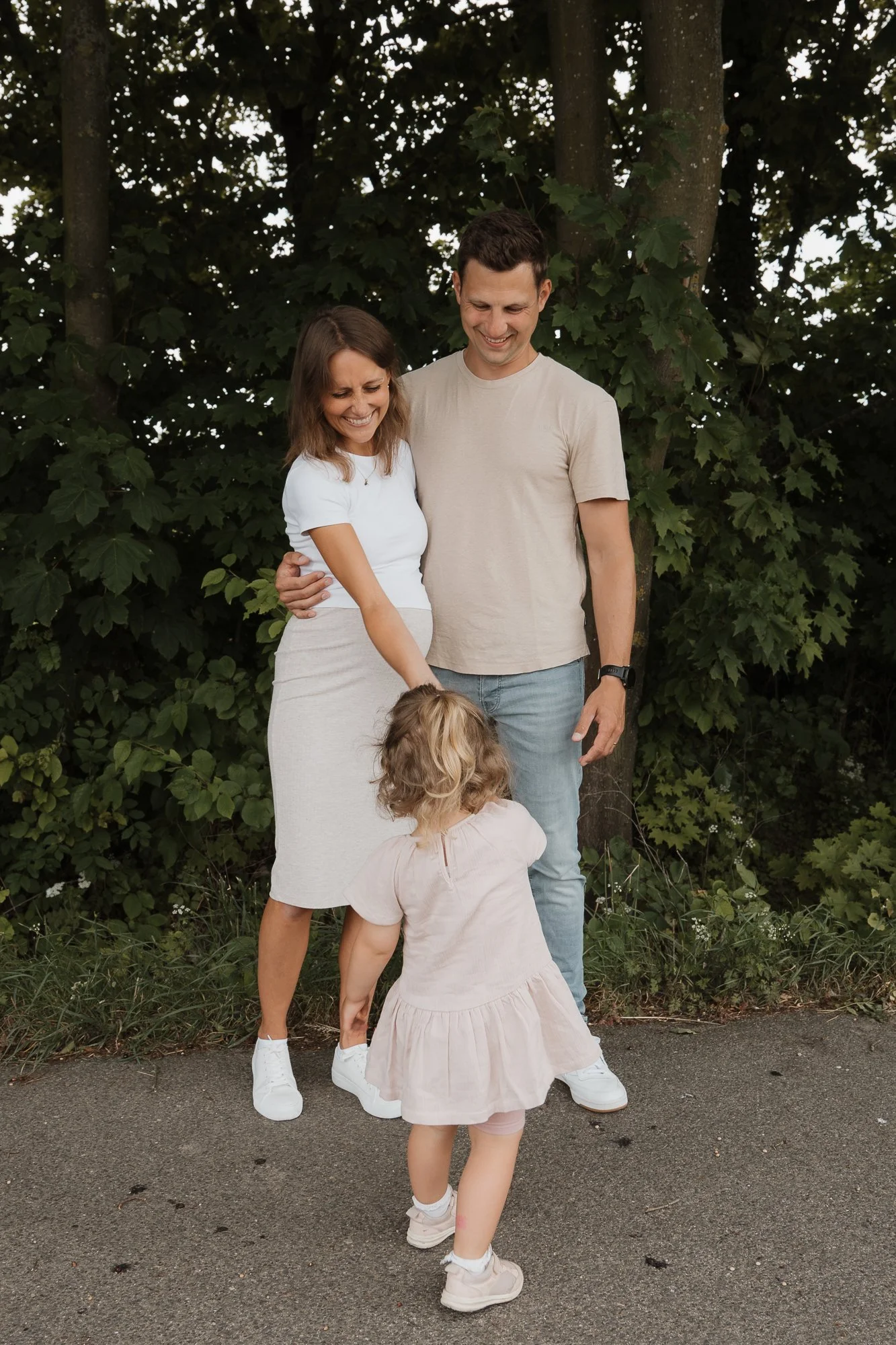 Familie mit zwei Erwachsenen und zwei Kindern, die draußen vor Bäumen stehen und lachen.