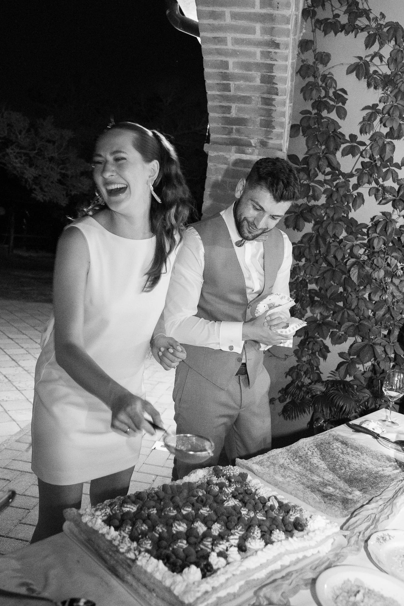 Ein lachendes Paar bei einer Geburtstagsparty oder Feier, mit einem Kuchen und Geschenken auf einem Tisch im Freien bei Nacht.