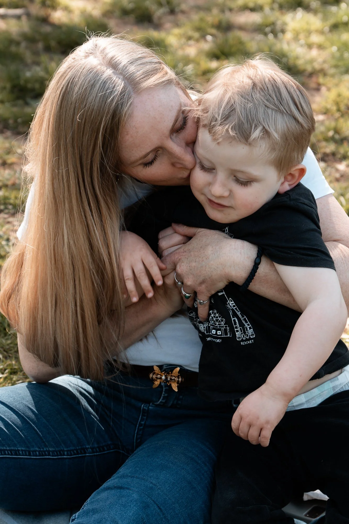 Eine Frau umarmt und küsst einen Jungen draußen auf einer Wiese.