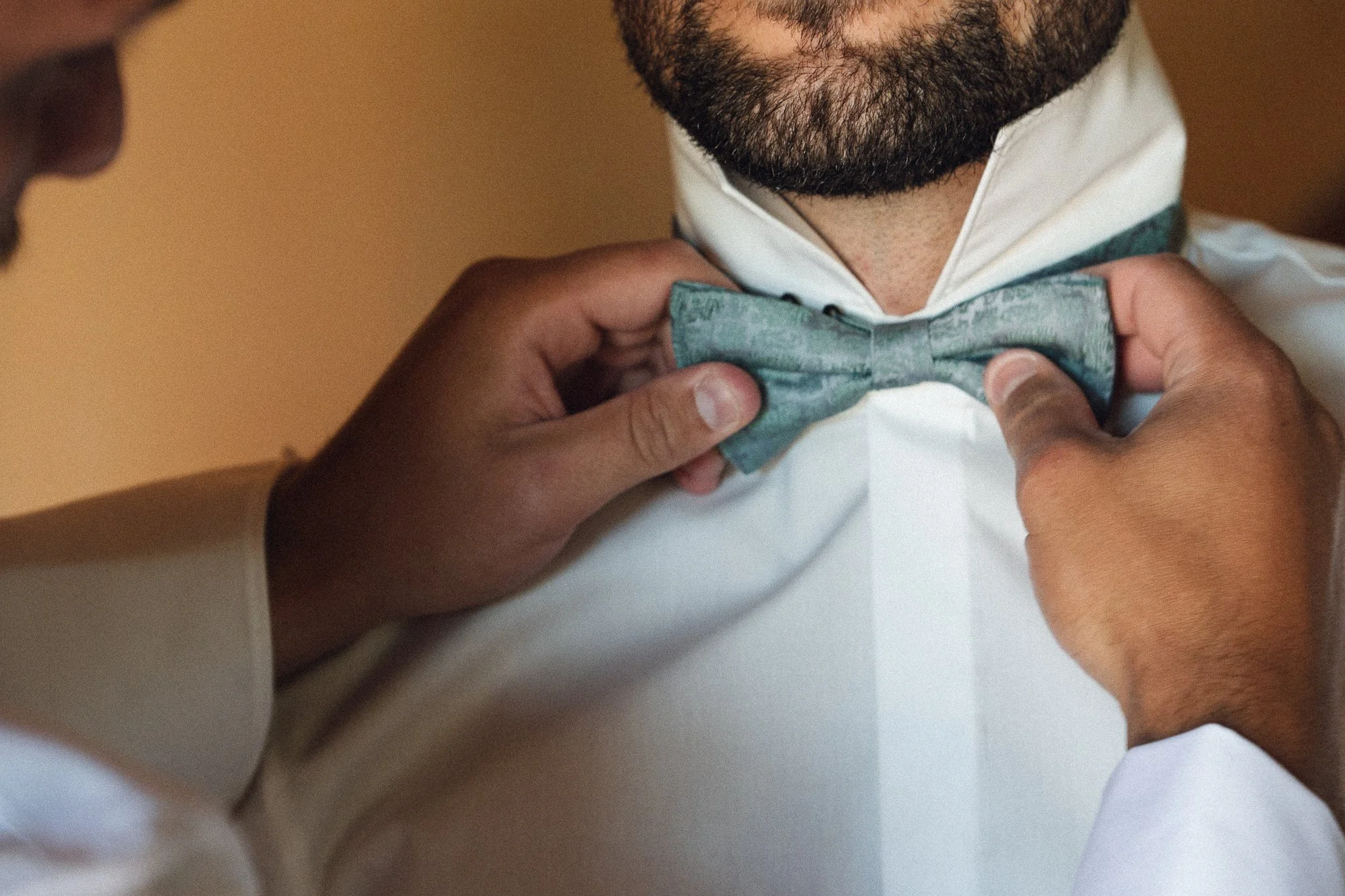 Ein Mann wird für eine formelle Veranstaltung mit einem gestärkten weißen Hemd und einer grauen Fliege vorbereitet.