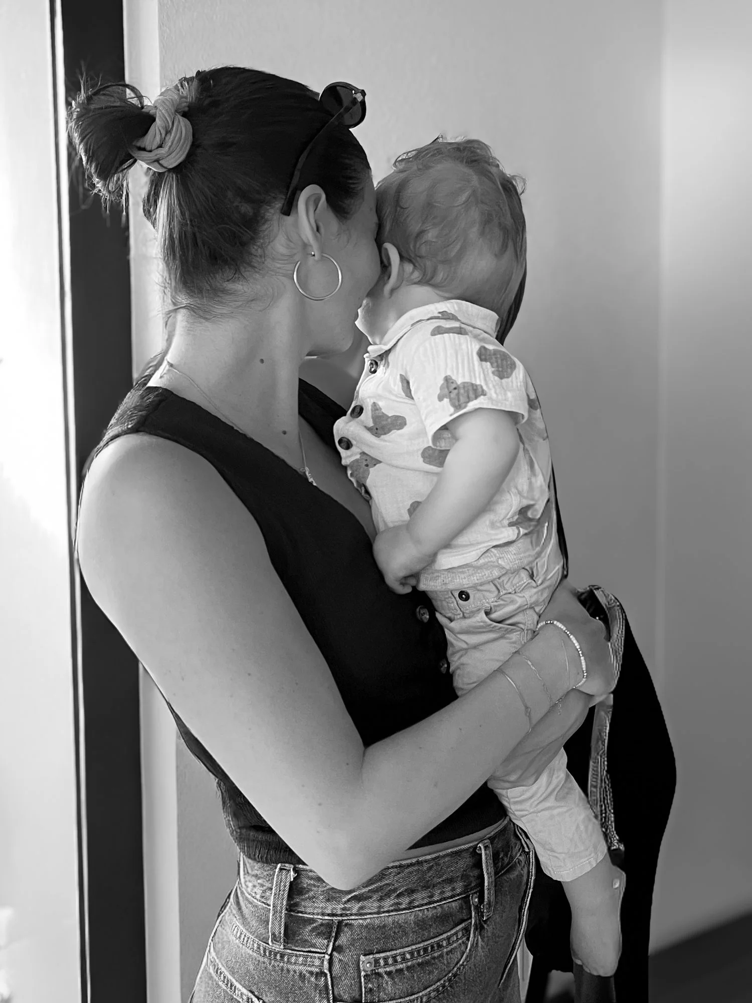 Eine Frau hält ein Kind in ihren Armen, sie scheinen sich zu küssen oder zu umarmen, im Hintergrund eine Tür und eine weiße Wand.