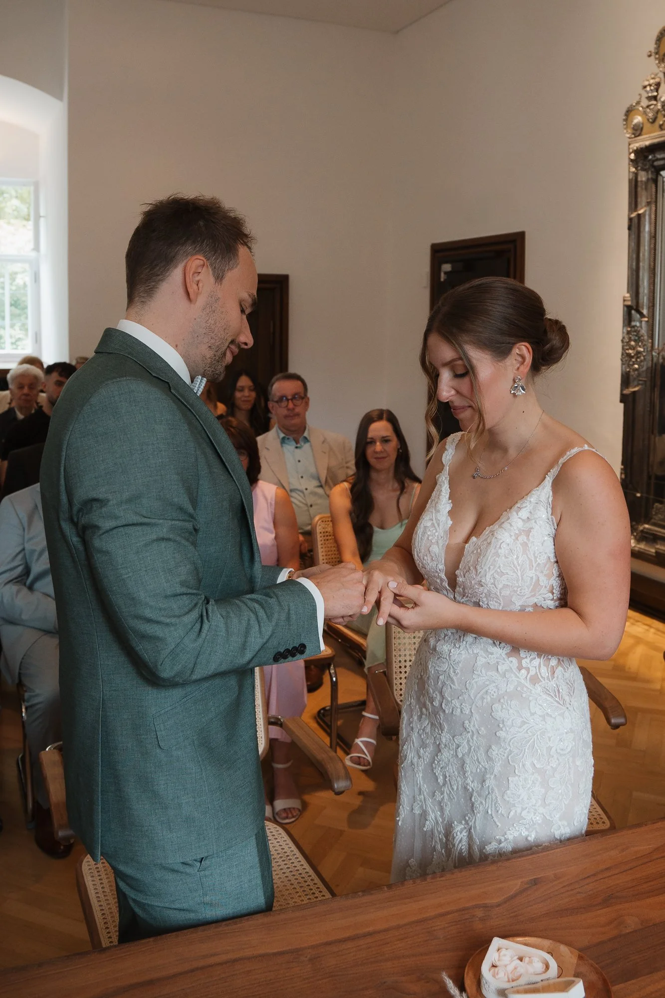 Ein Paar bei einer Eheschließung, der Bräutigam steckt einem Brautring an die Hand der braut in einem festlichen Raum.