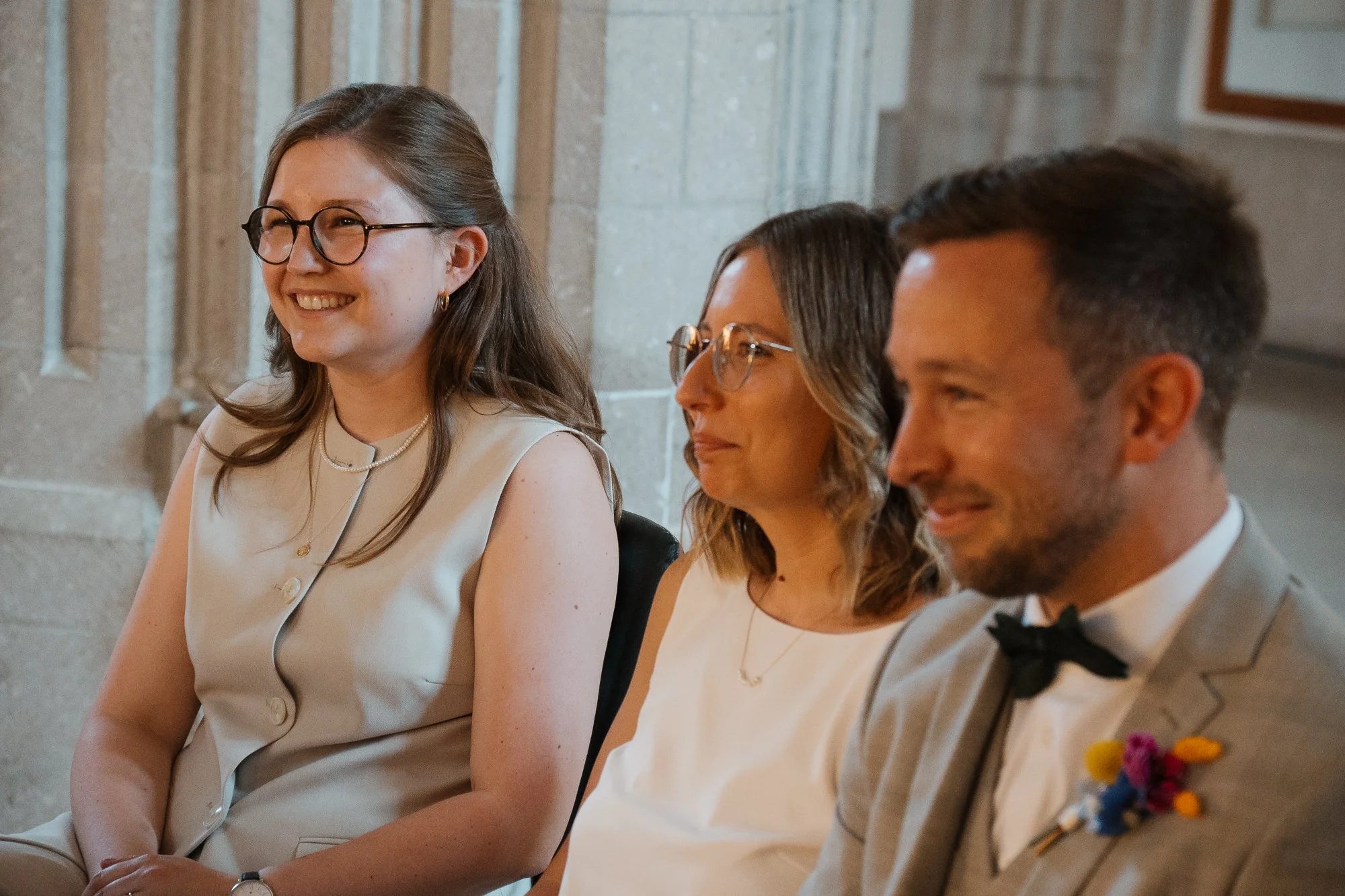 Drei Menschen sitzen bei einer formellen Veranstaltung, lächeln und tragen elegante Kleidung.