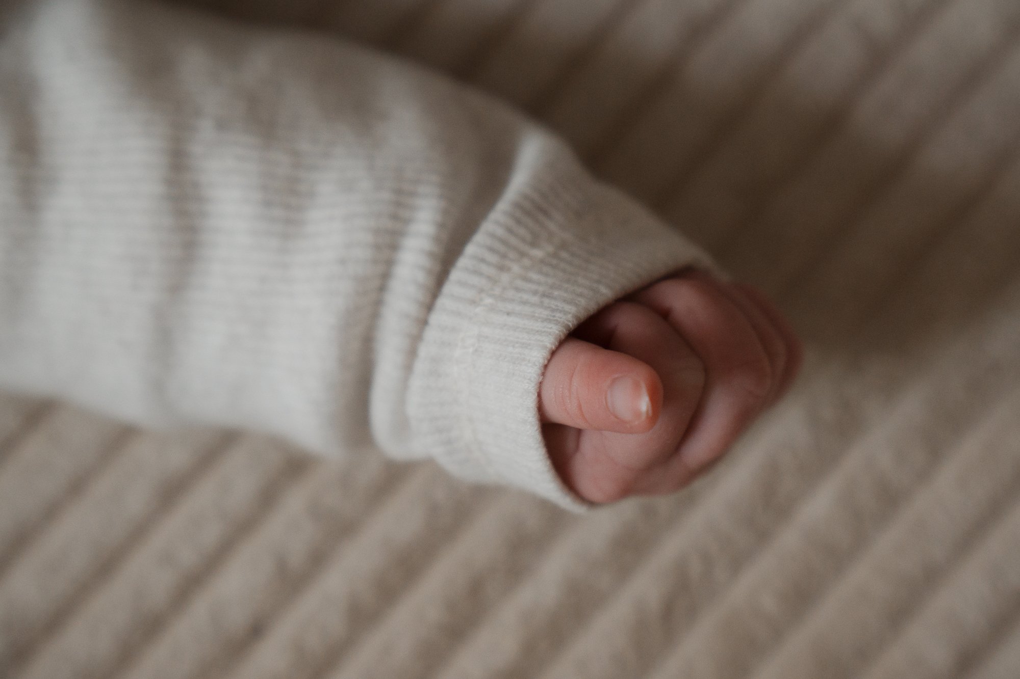 Nahaufnahme eines Babys, das die Faust ballt, in einem beige gestreiften Pullover.