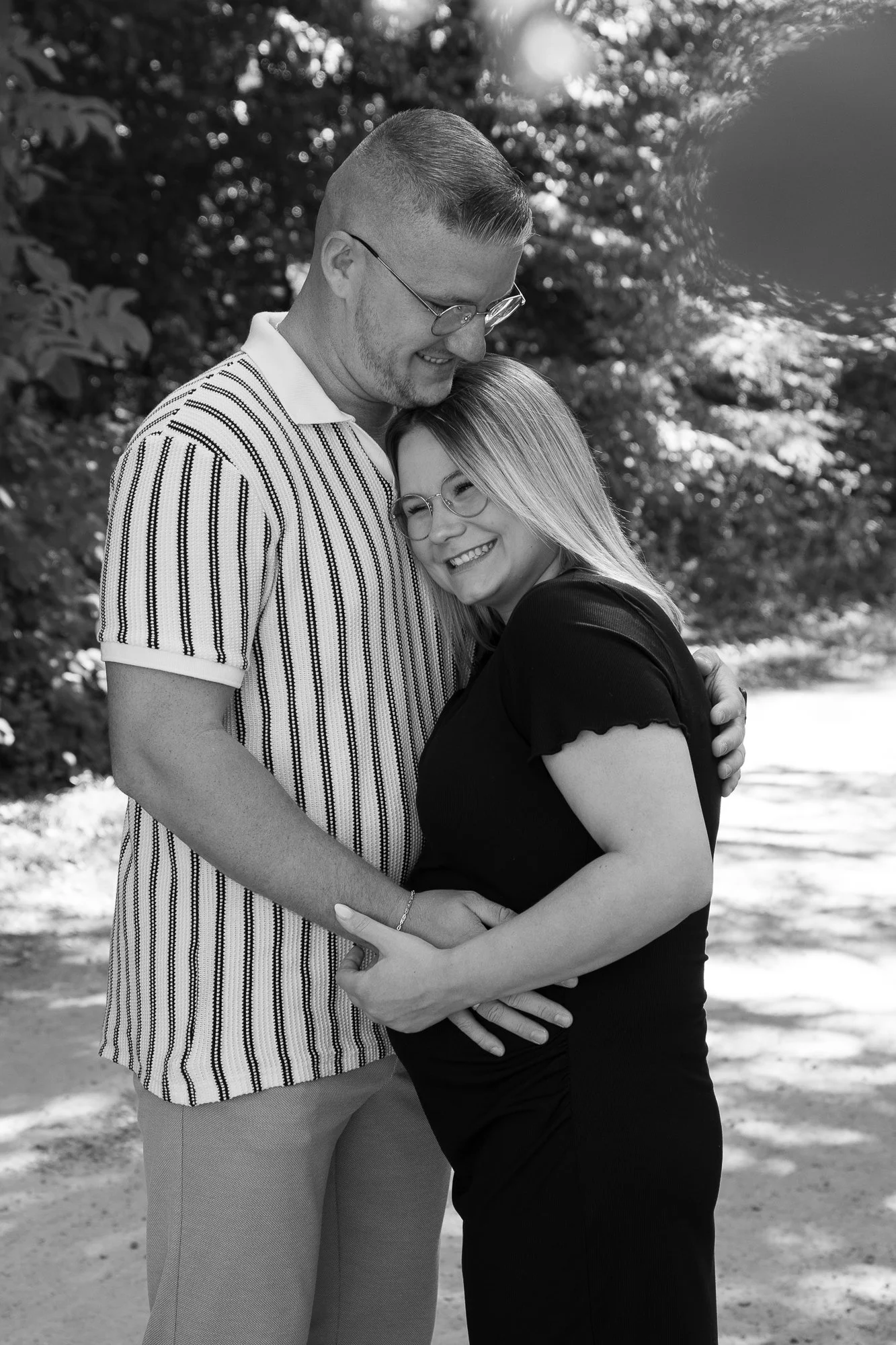Ein lachendes Paar umarmt sich im Freien, im Hintergrund Bäume, in Schwarz-Weiß
