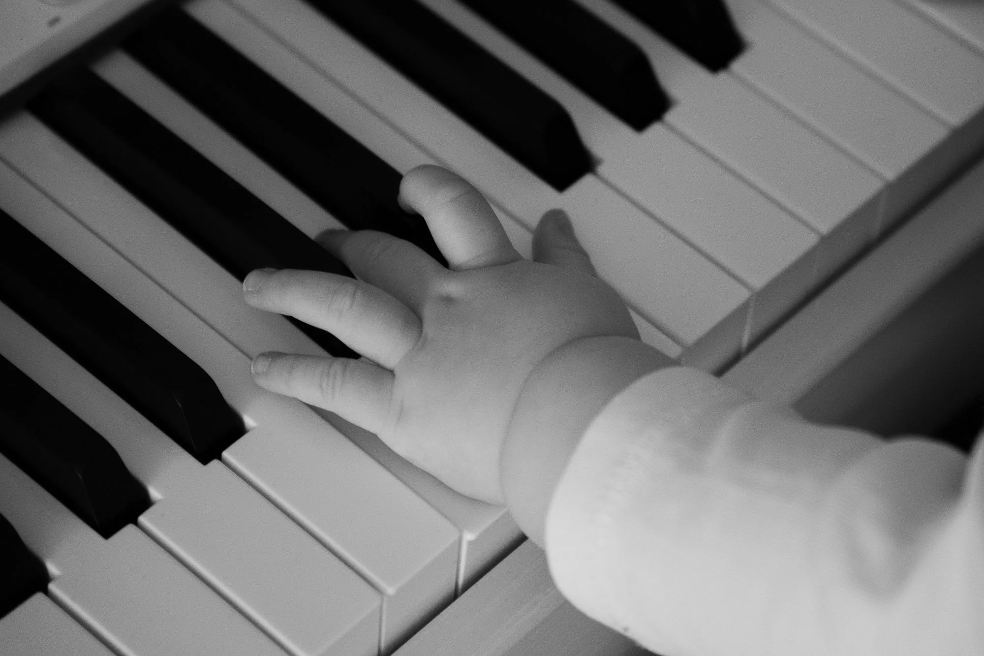 Ein Kind hat die Hand auf die Tasten eines Klaviers gelegt, schwarze und weiße Tasten sind sichtbar.