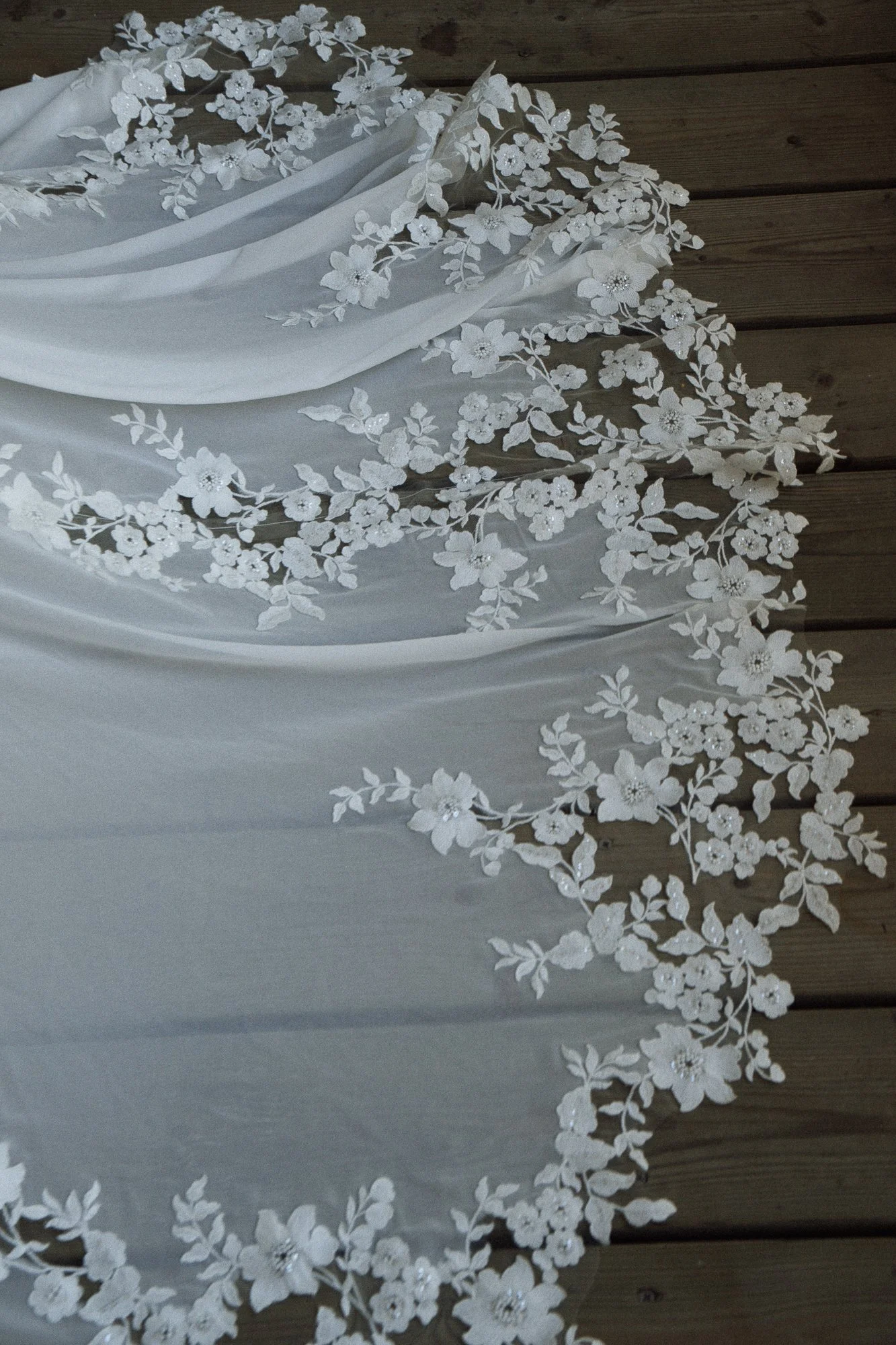 Weiße Brautjungfern-Schleier mit Blumendetails, auf Holzfußboden liegend.