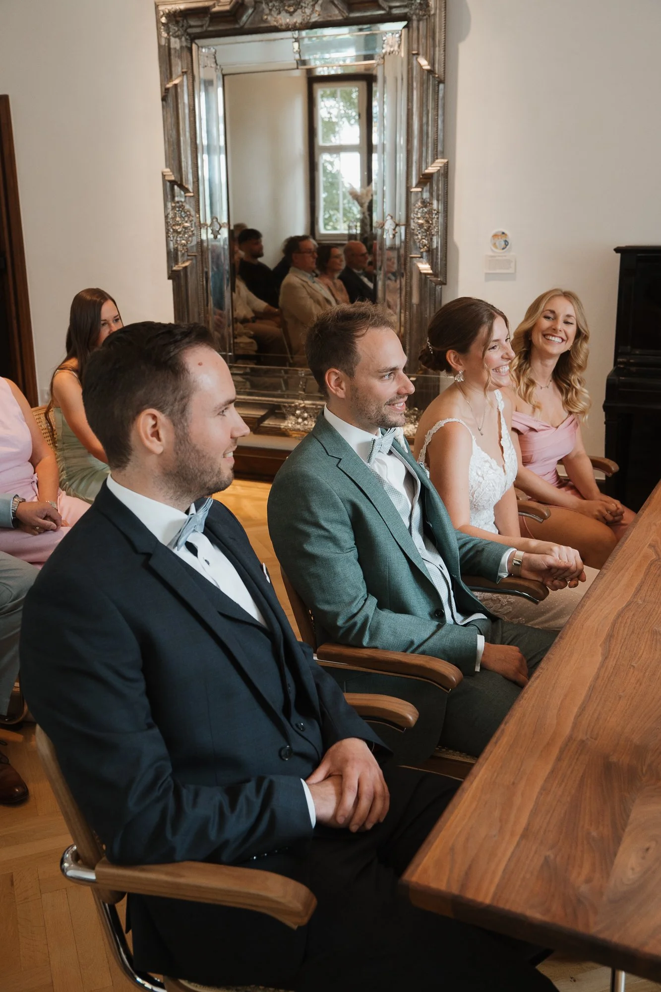 Eine Gruppe von Menschen bei einer Hochzeitszeremonie, die im Raum sitzen und sich lächelnd anschauen.