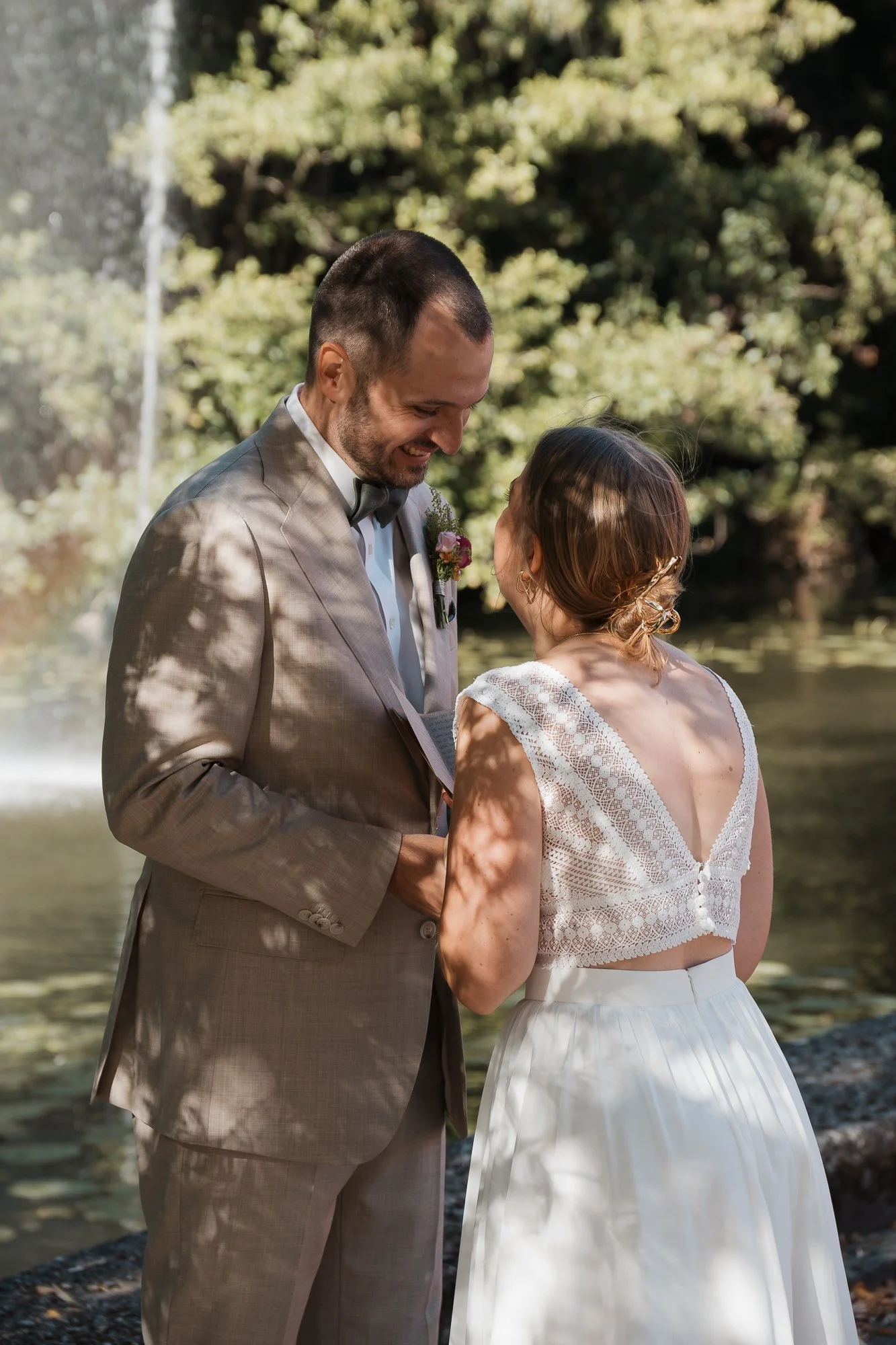 Ein Brautpaar steht sich in der Natur gegenüber, lächelt sich an und hält Händchen während einer Zeremonie im Freien.