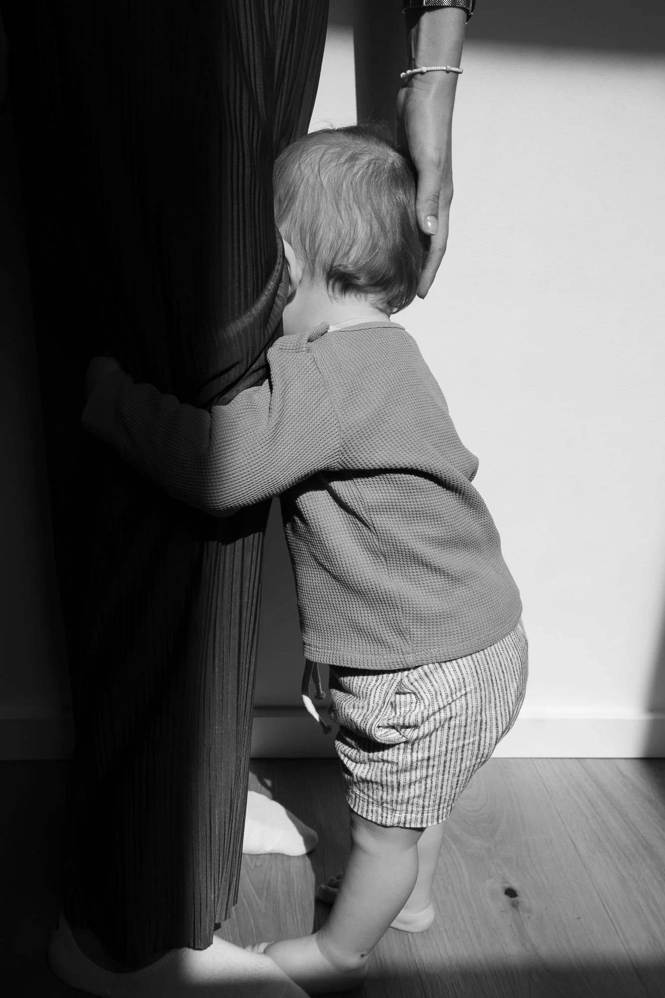 Ein kleiner Junge umarmt eine erwachsene Person. Das Bild ist schwarz-weiß, und der Junge trägt ein langärmeliges Hemd und Short.