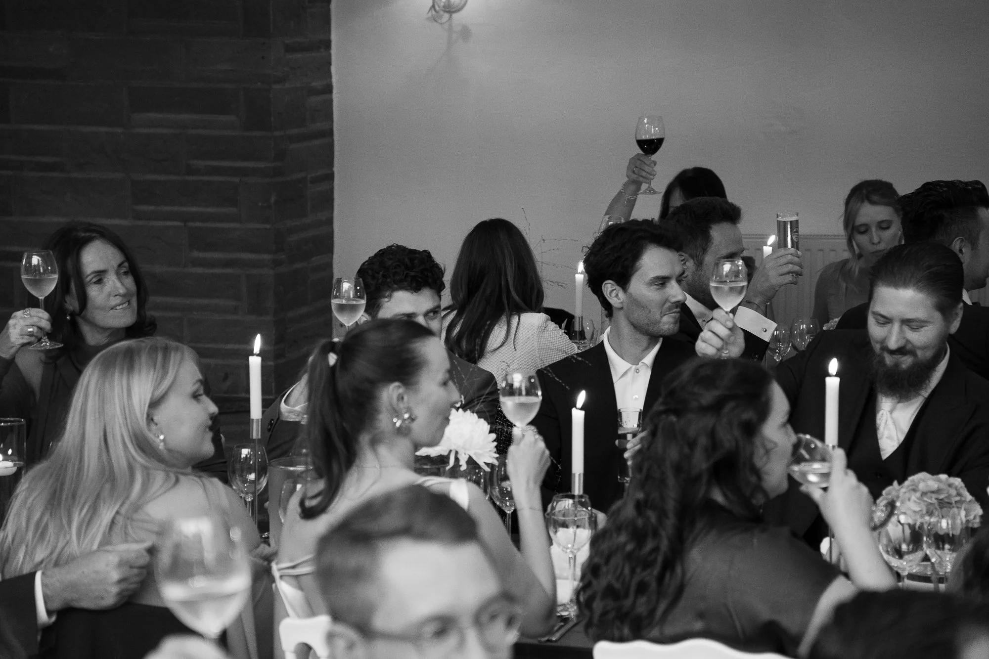 Menschen bei einer Feier mit Kerzen, einigen mit Weingläsern in der Hand, in einer festlichen Atmosphäre