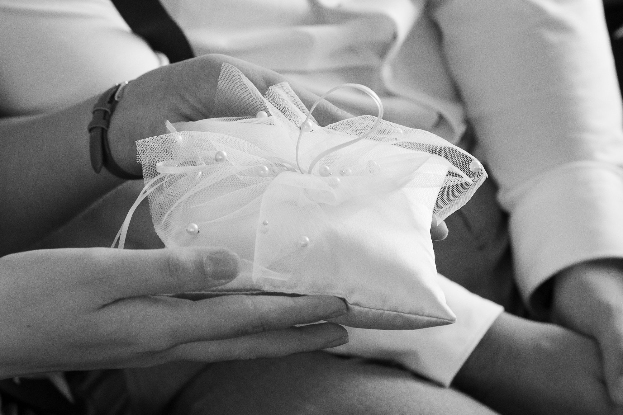 Nahaufnahme einer Person, die eine Brautkissen mit Tüll und Perlen hält, vermutlich bei einer Hochzeit.