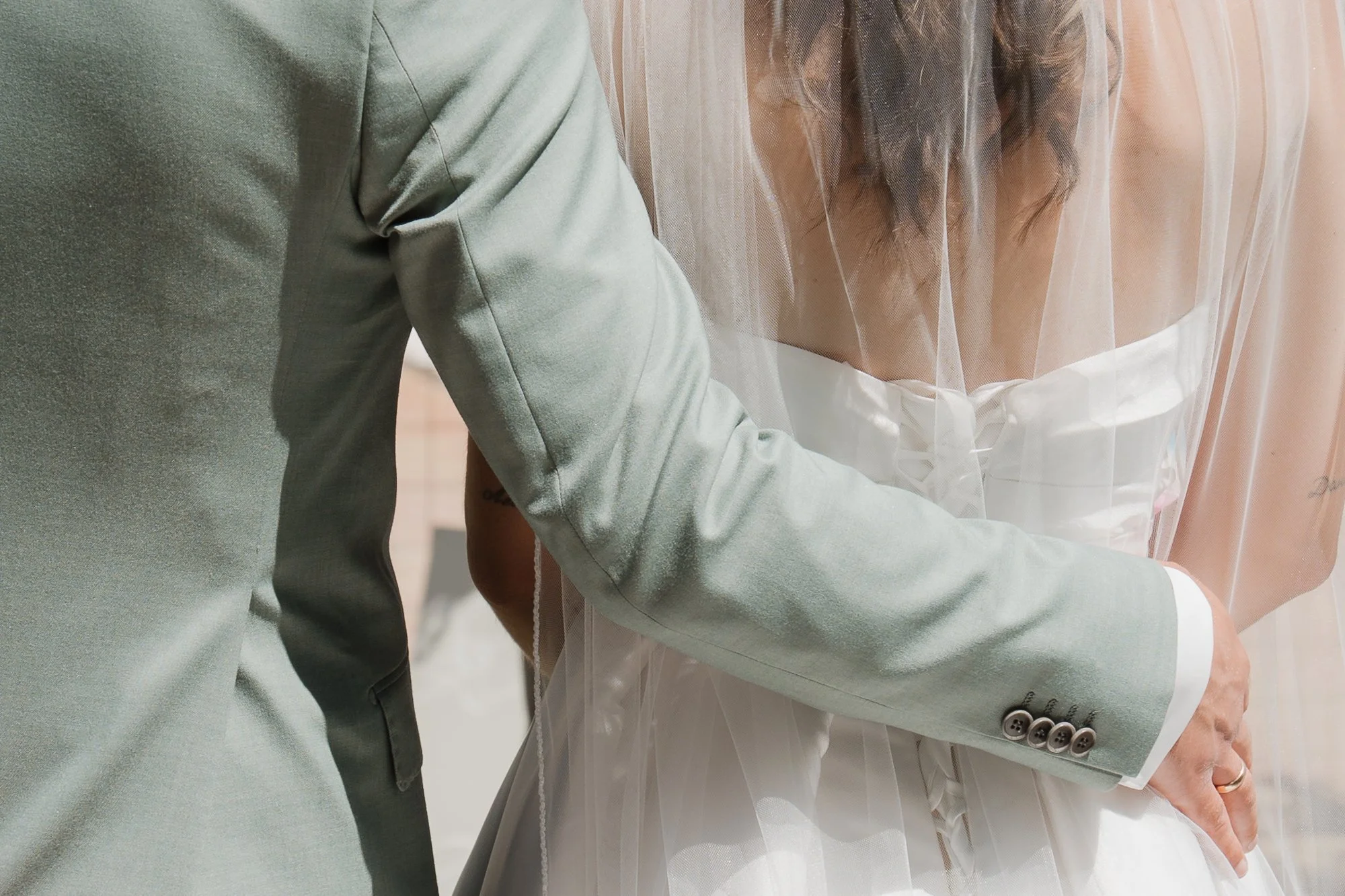 Nahaufnahme eines Paares bei der Hochzeit, das sich umarmt, mit Fokus auf die Hände und die Hochzeitskleidung.