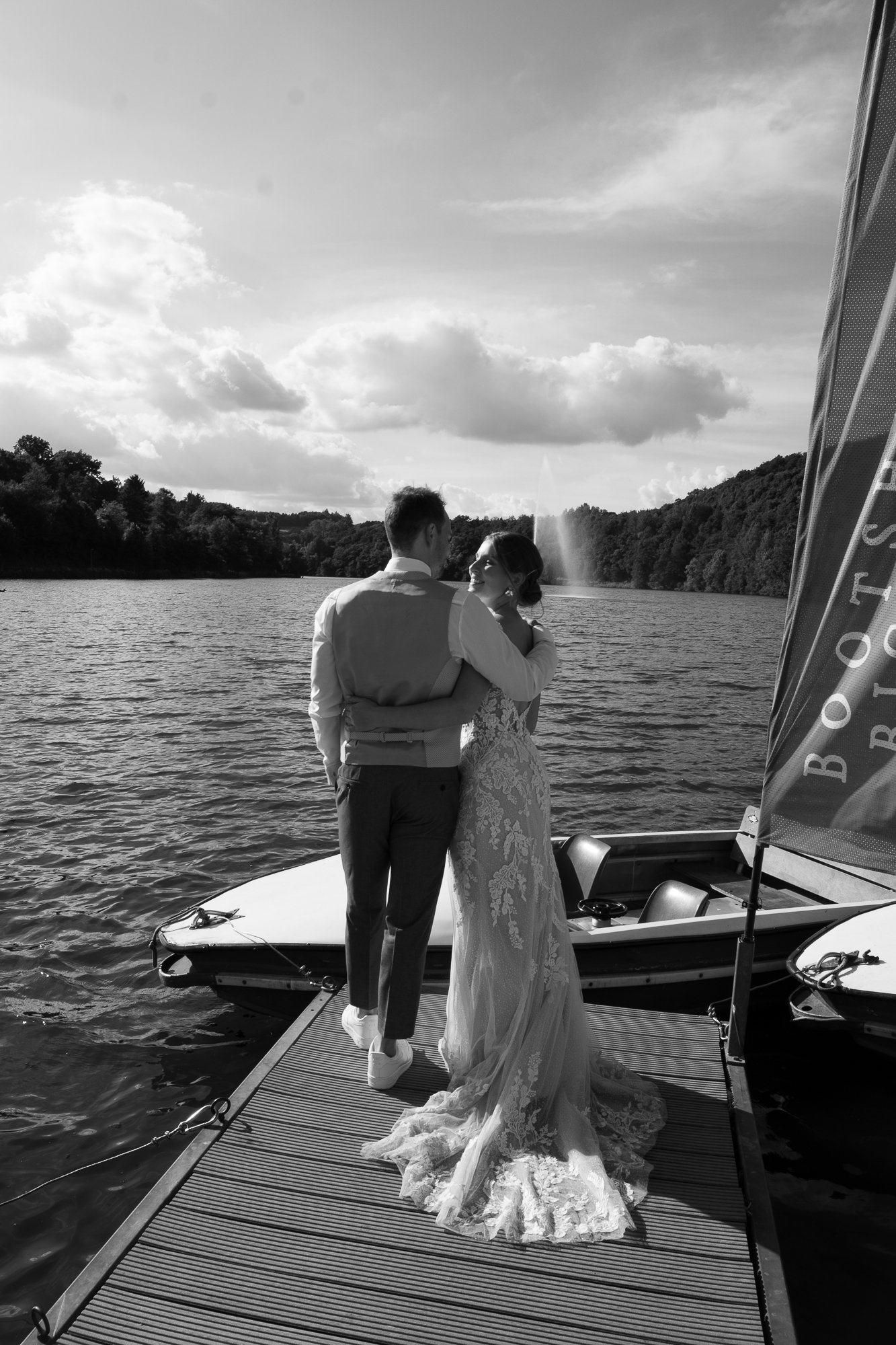 Ein Brautpaar auf einem Boot auf einem See, umgeben von Wasser, Bäumen und Himmel mit Wolken, in Schwarz-Weiß, romantisch.