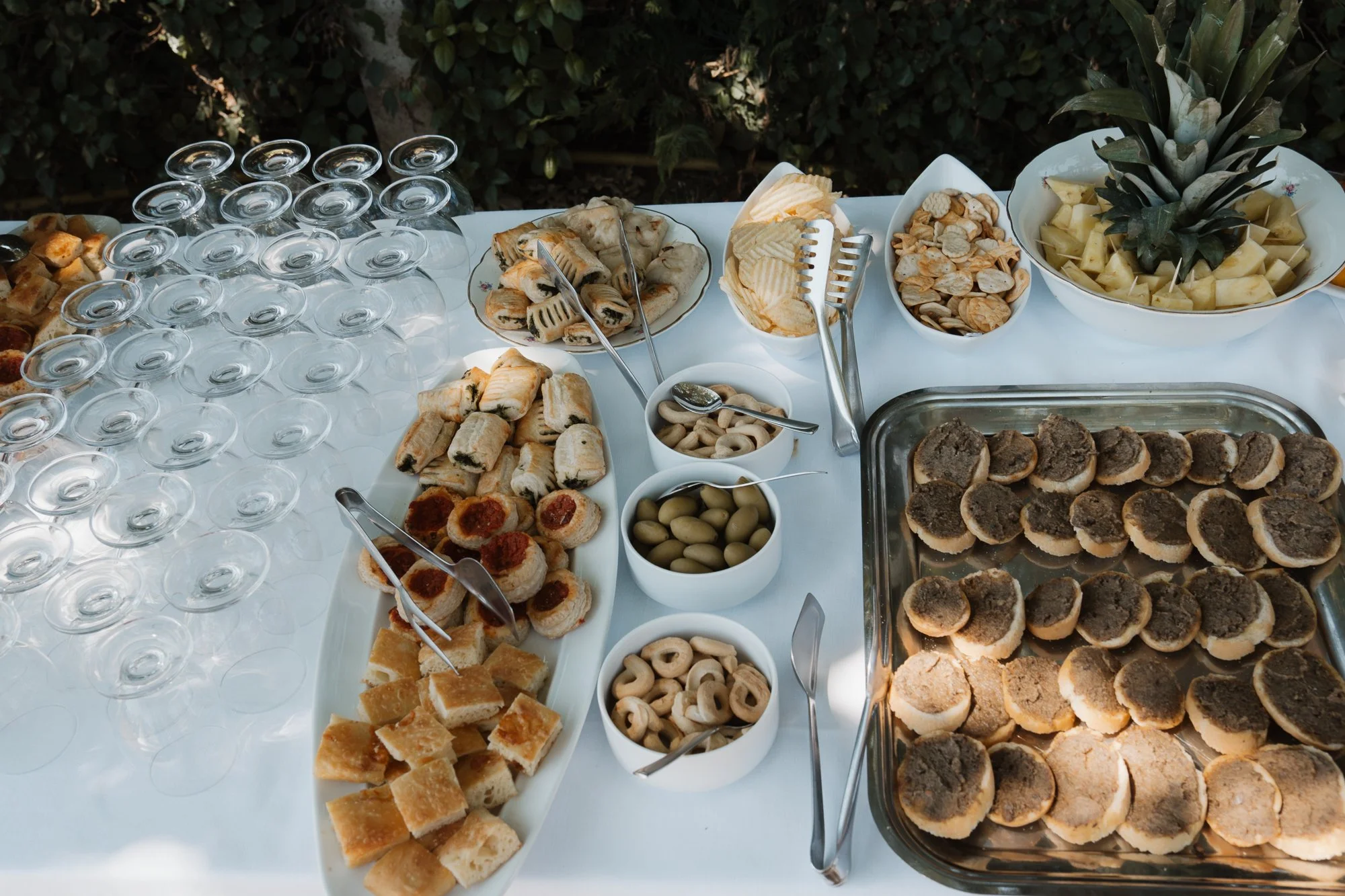 Büffet mit verschiedenen Canapés, Keksen, Oliven, Chips, und Fruchtstücken, mit leeren Weingläsern auf einem weißen Tisch.