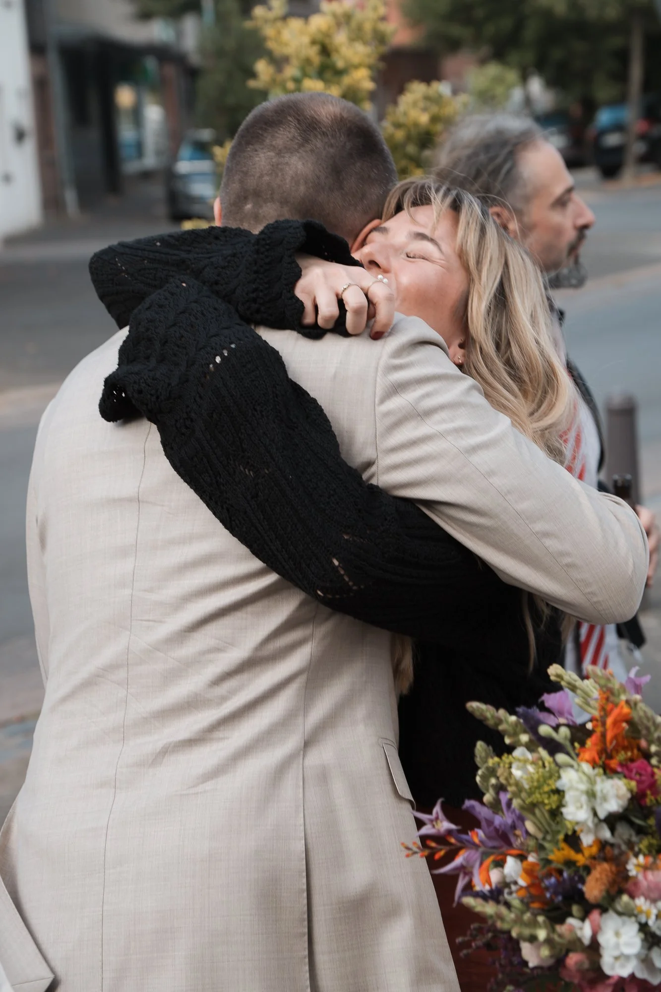 Zwei Menschen umarmen sich liebevoll auf der Straße, eine Frau hat die Augen geschlossen und lächelt.