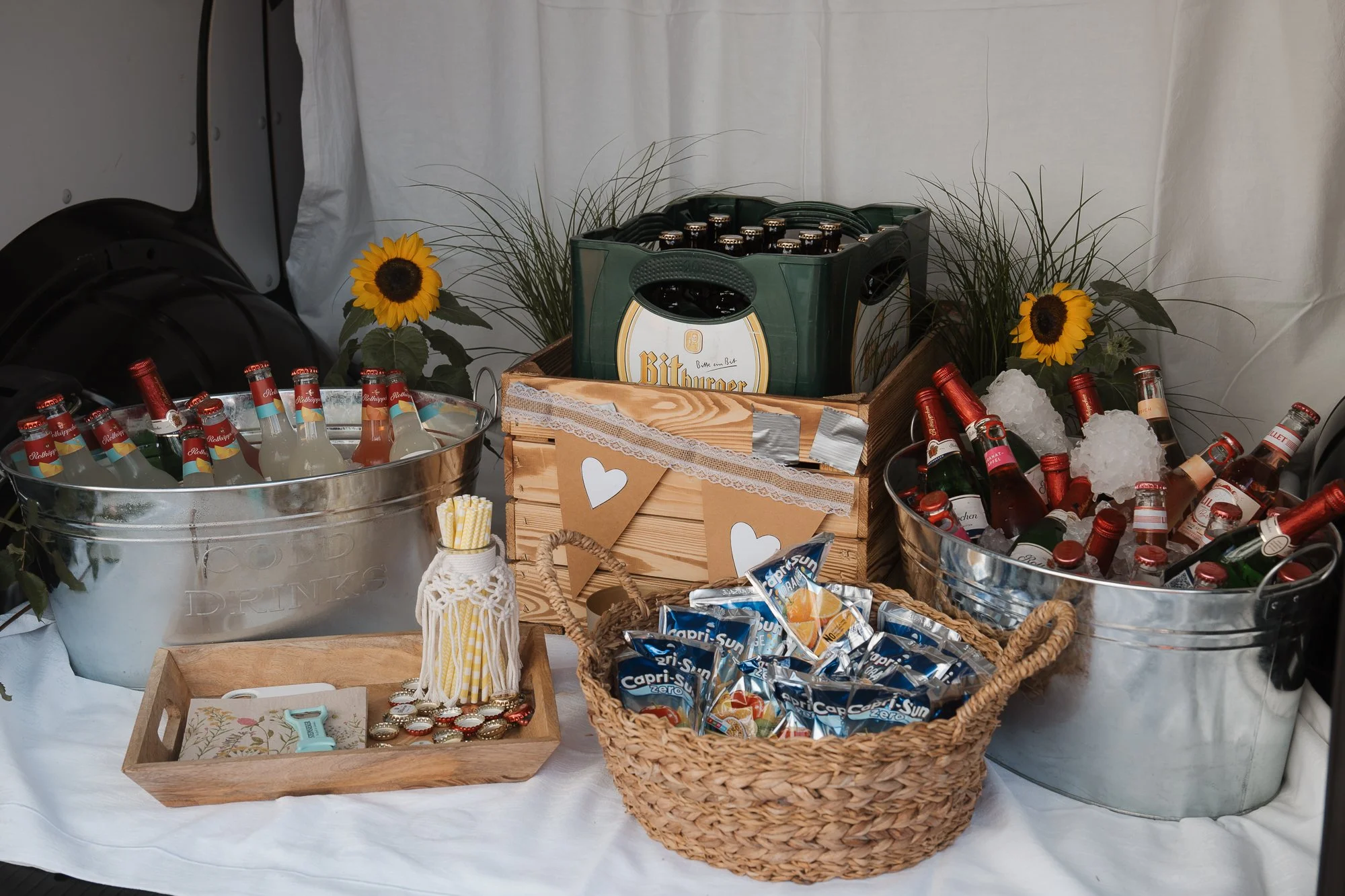 Getränkestation mit Bier, alkoholischen Getränken, Wasser, Snacks und Dekoration, inklusive Sonnenblumen und grünen Pflanzen.