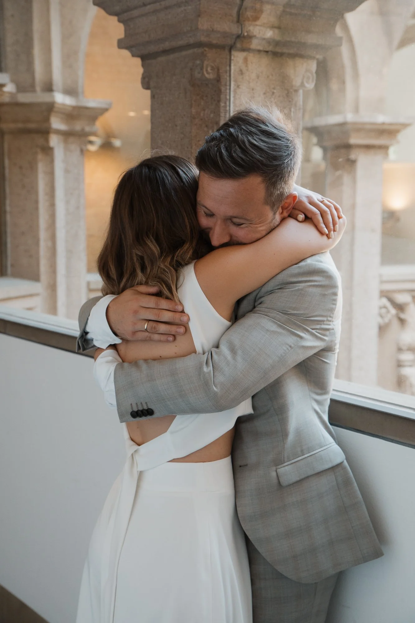 Zwei Menschen umarmen sich liebevoll, im Hintergrund antike Säulen.