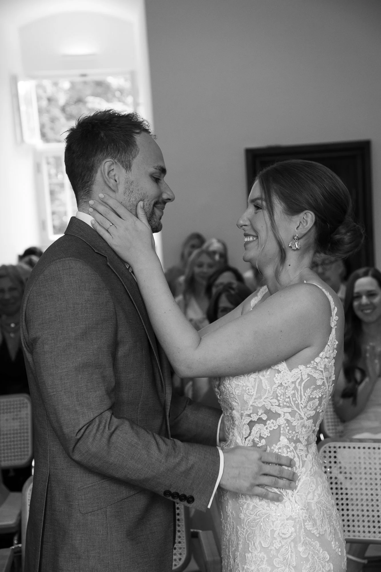 Ein Brautpaar bei ihrer Zeremonie, die sich liebevoll anschauen, während die Gäste im Hintergrund zuschauen.