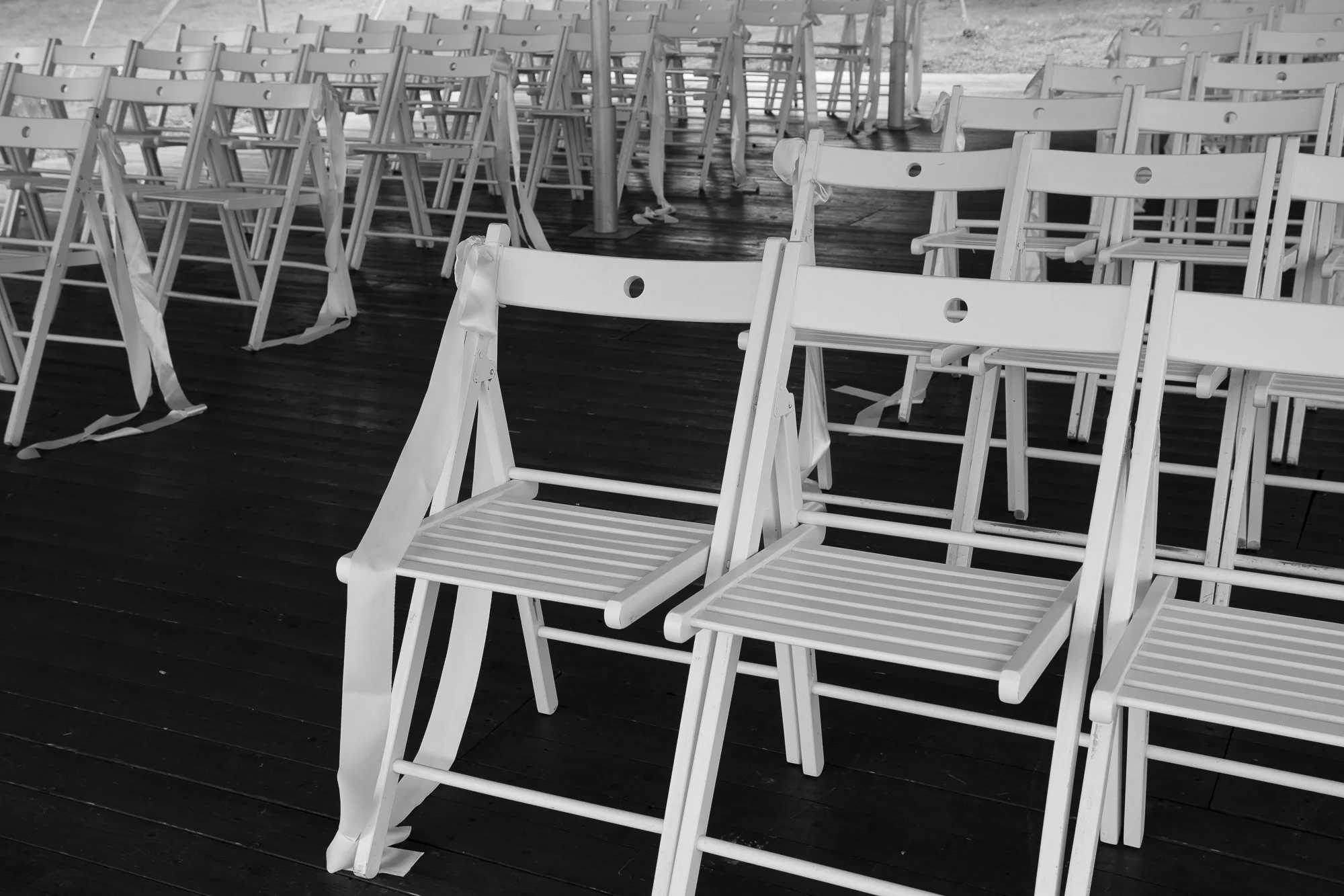Leere weiße Klappstühle auf einem dunklen Holzboden, einige mit Seitenbändern befestigt.