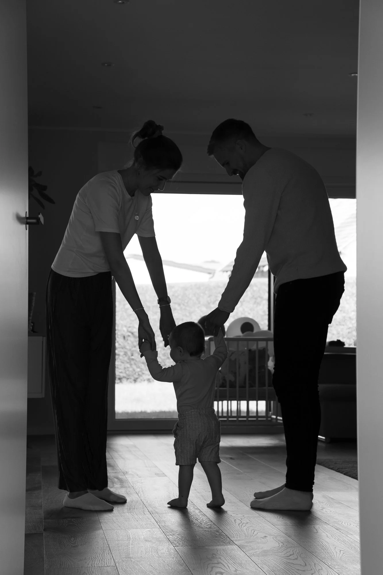 Ein Kind lernt von seinen Eltern zu laufen, während sie sich im Haus an einem Fenster befinden.