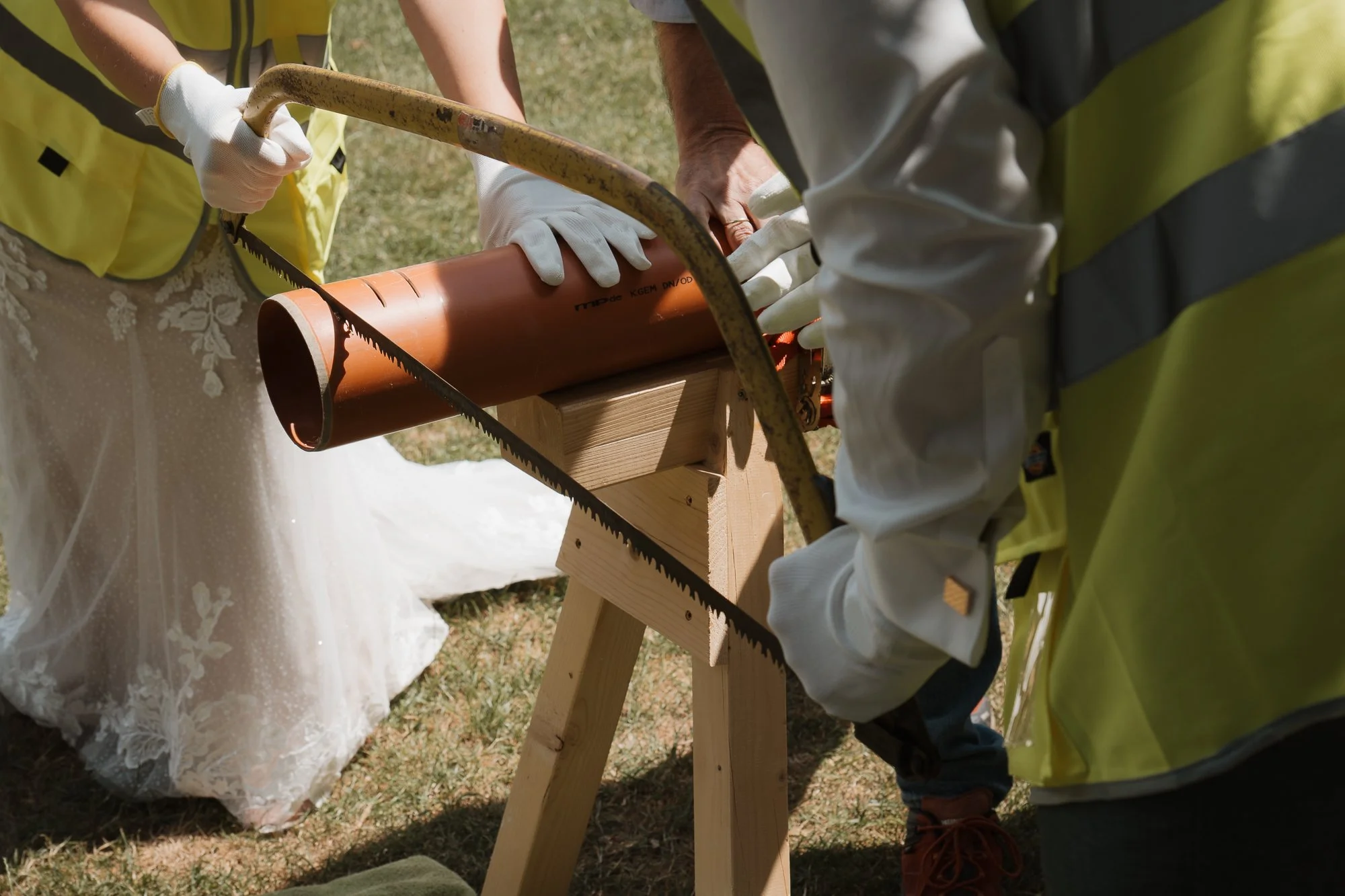 Menschen bei einem Bauprojekt arbeiten an einem Abflussrohr, das auf einem Holzständer fixiert ist, während sie eine Handsäge benutzen.