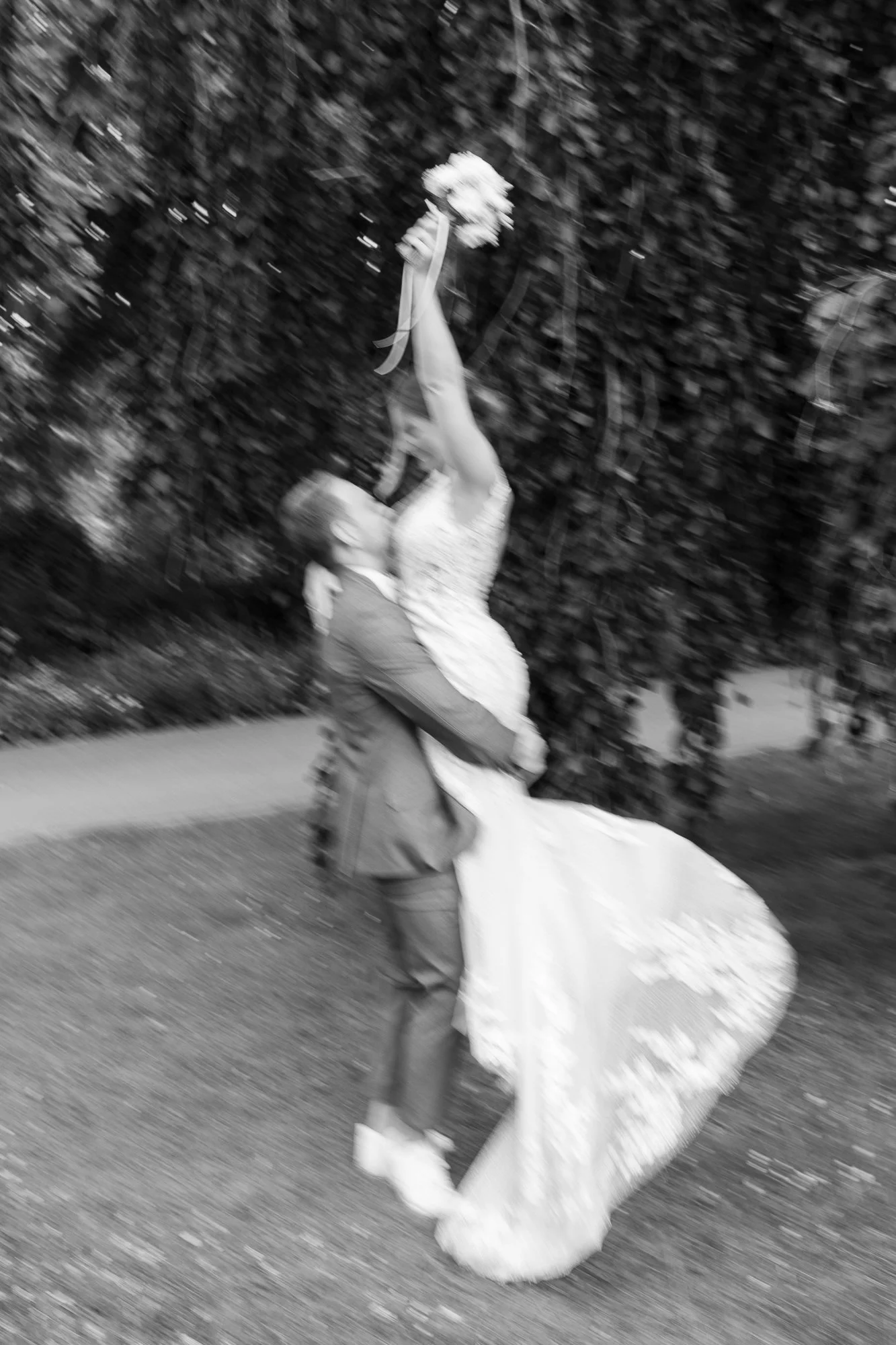 Ein brautspaar bei einer Hochzeitsfeier im Freien, mit dem Mann, der die Braut hält, während sie den Arm hebt, um einen Blumenstrauß zu greifen.