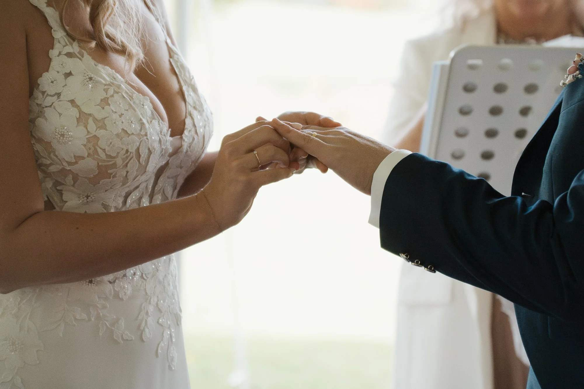 Ein Brautpaar tauscht Ringe während einer Hochzeitszeremonie, die Frau trägt ein Spitzenkleid, der Mann einen dunklen Anzug.