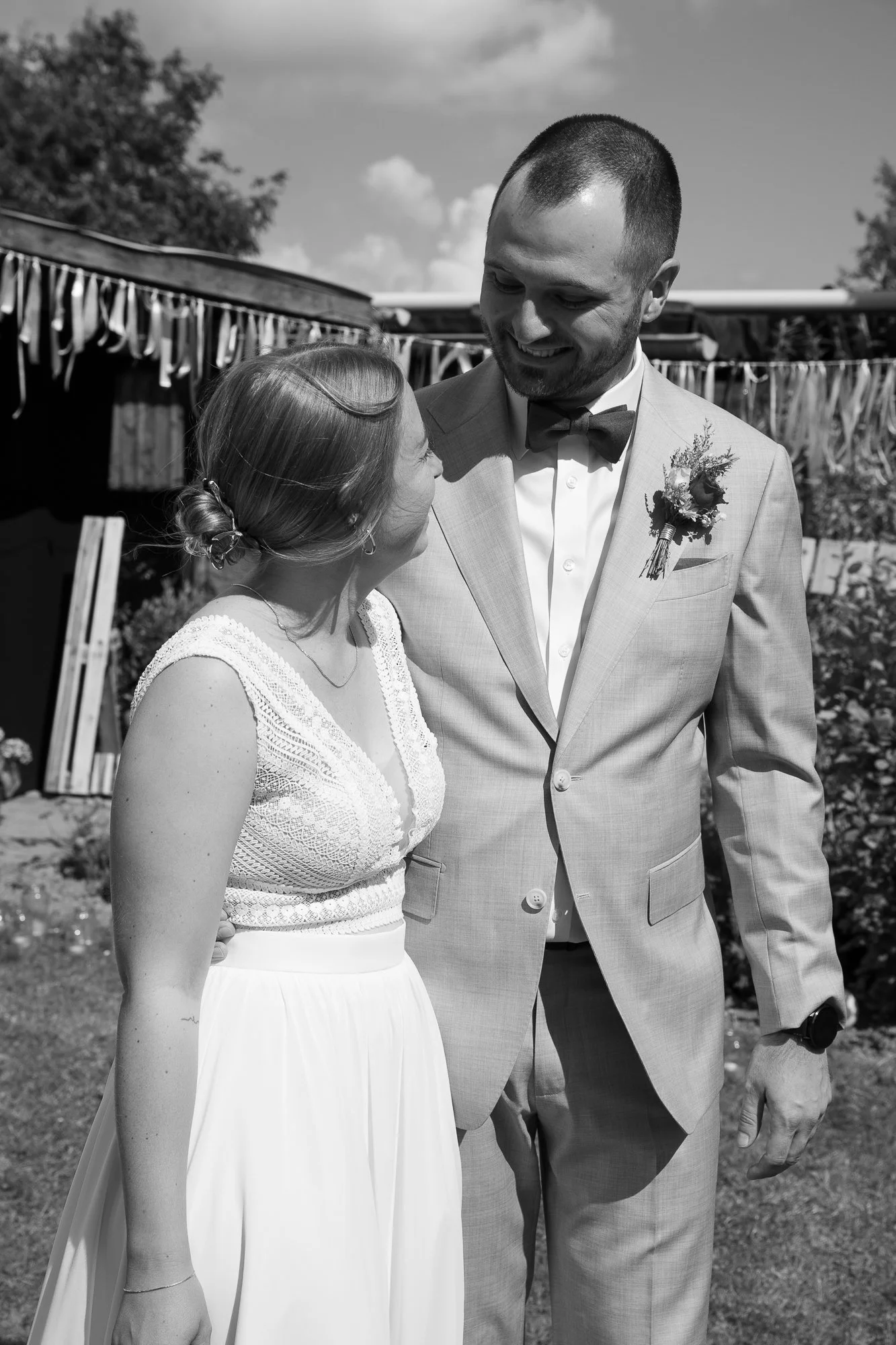 Ein Mann und eine Frau stehen sich bei einer Hochzeit im Freien gegenüber und lächeln sich an.
