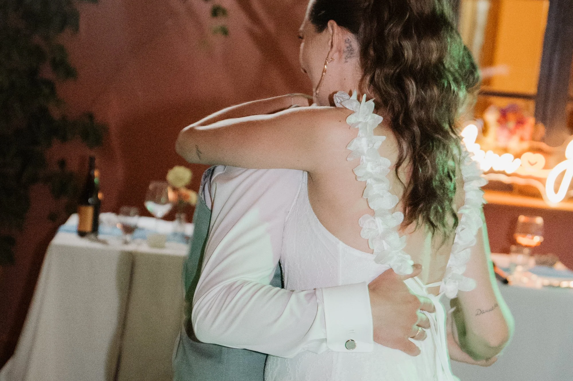 Ein Paar tanzt bei einer Hochzeit, umarmt sich und trägt festliche Kleidung, mit einer Tischdekoration im Hintergrund.