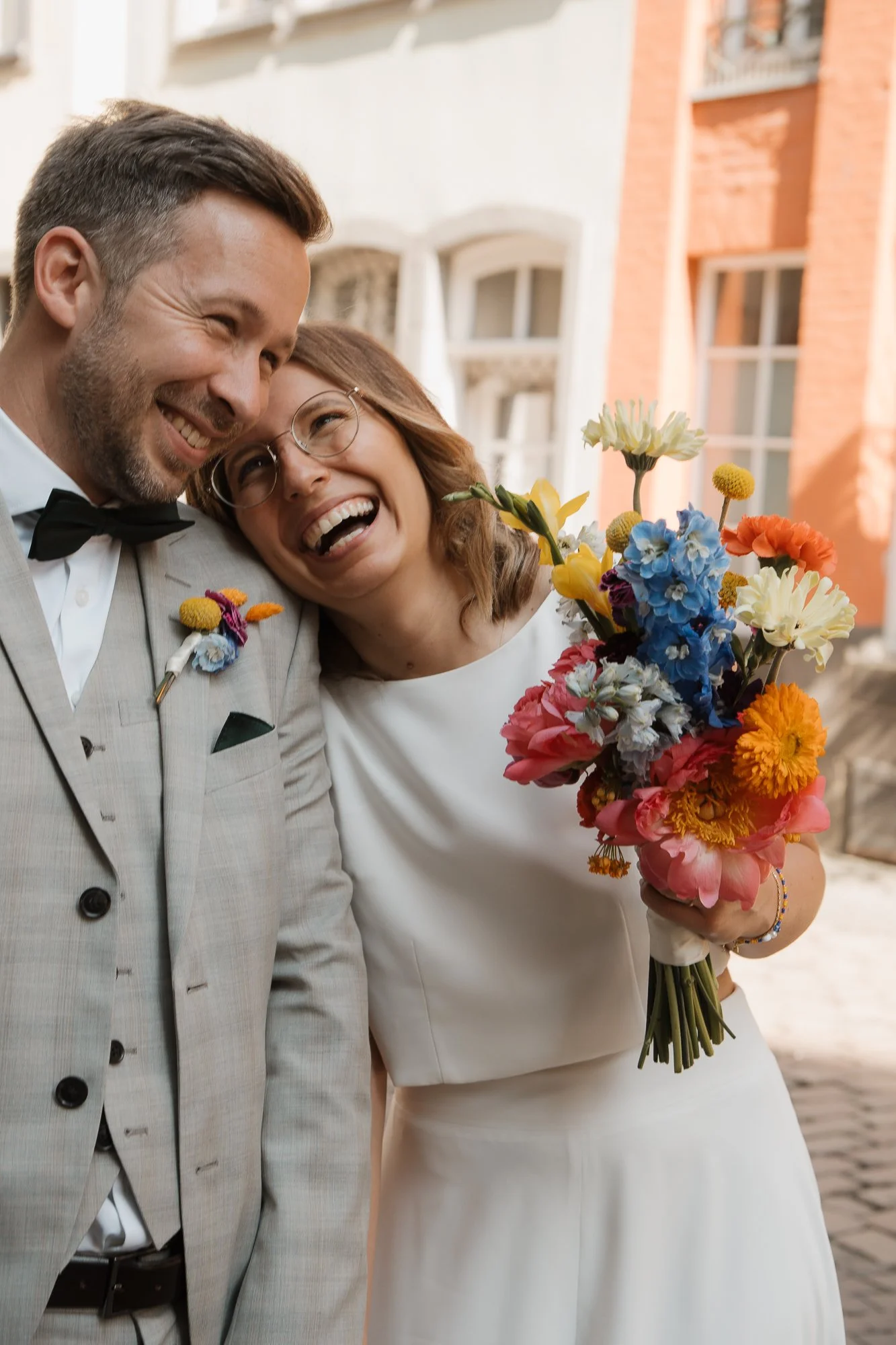 Ein lachendes Brautpaar auf einer Hochzeit, die Braut hält einen bunten Blumenstrauß.