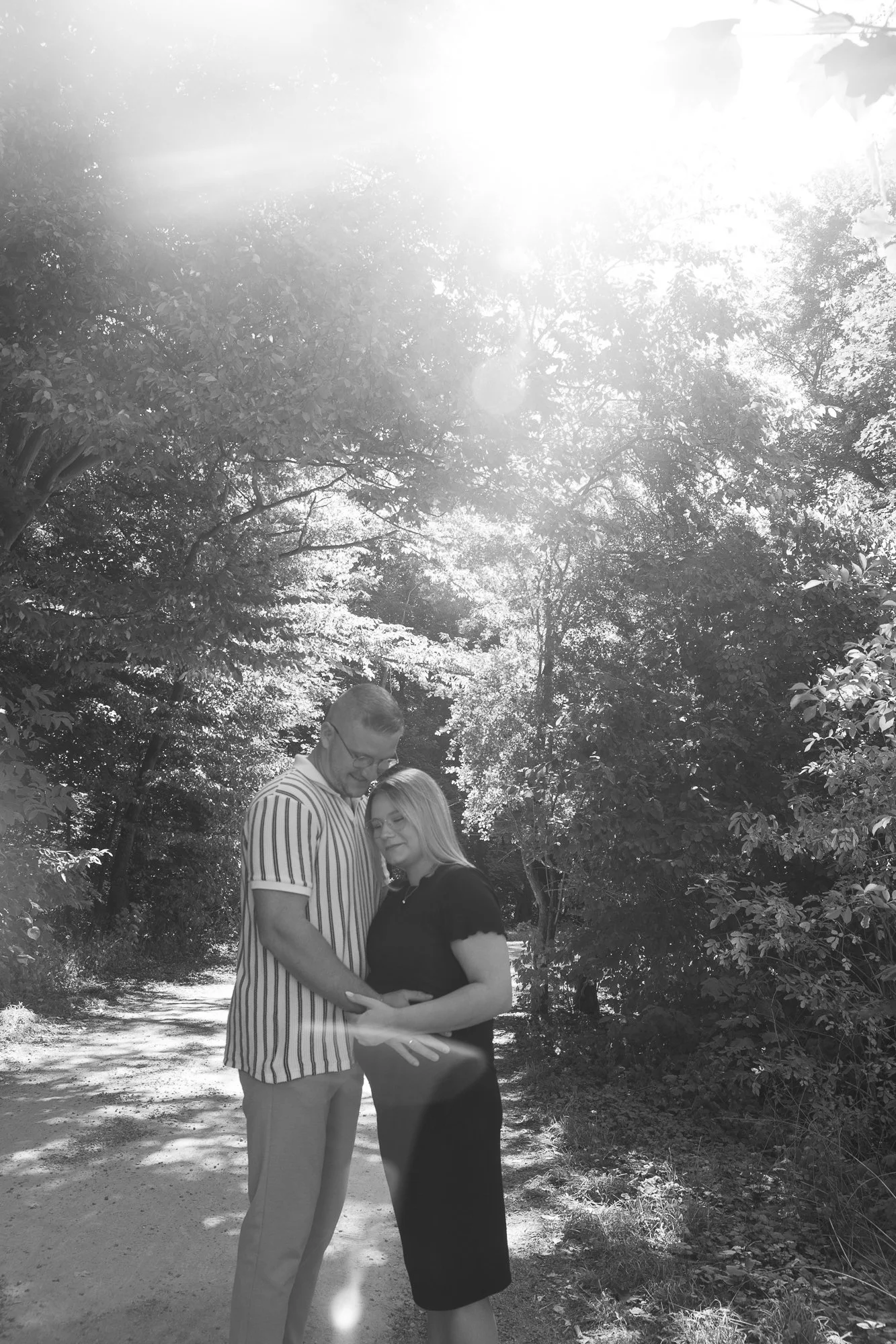 Ein Paar steht liebevoll in einem Wald, sie umarmen sich und schauen sich glücklich an, Sonnenlicht dringt durch die Baumwipfel.