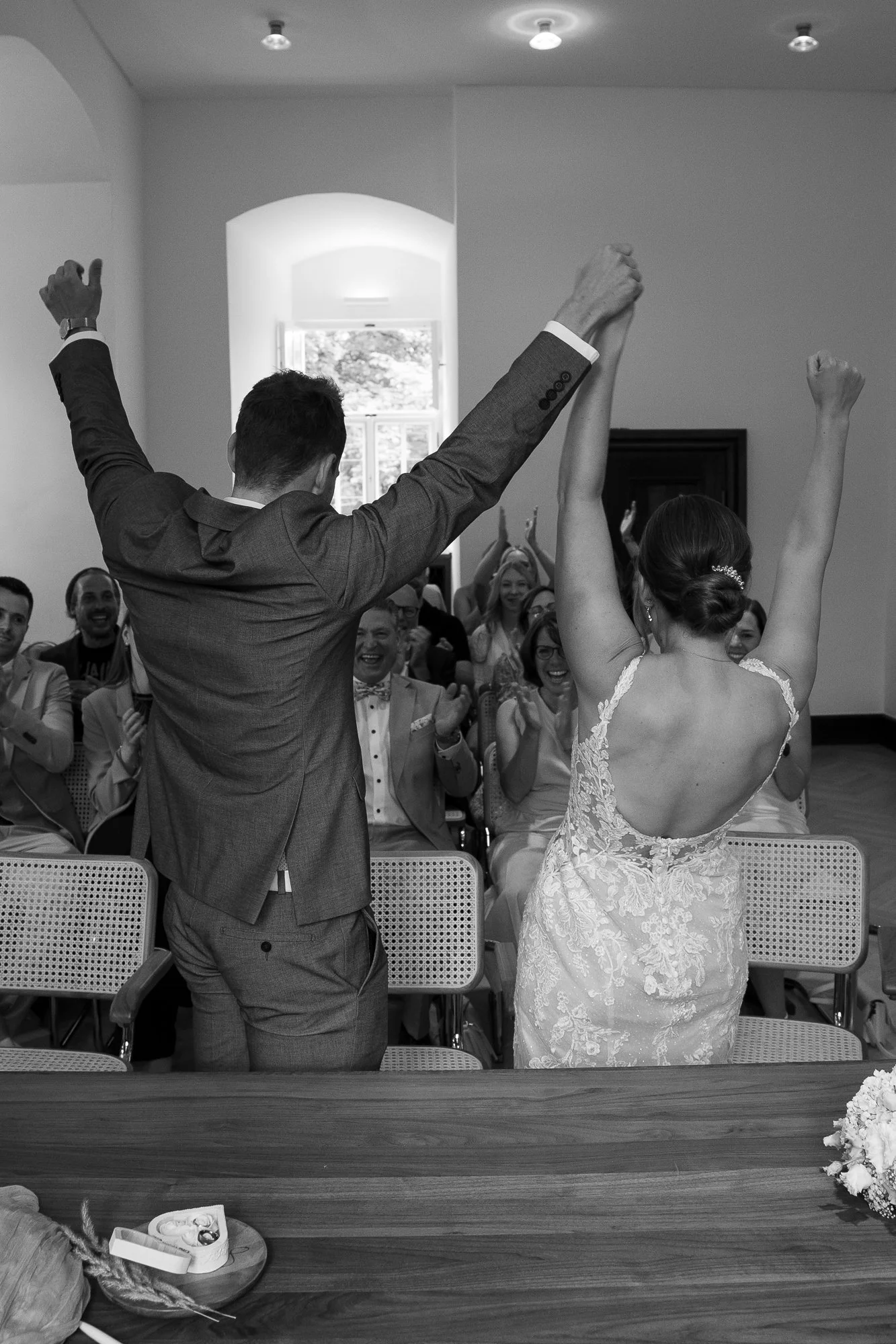 Braut und Bräutigam feiern bei ihrer Hochzeit im Saal, die Gäste applaudieren und lachen.