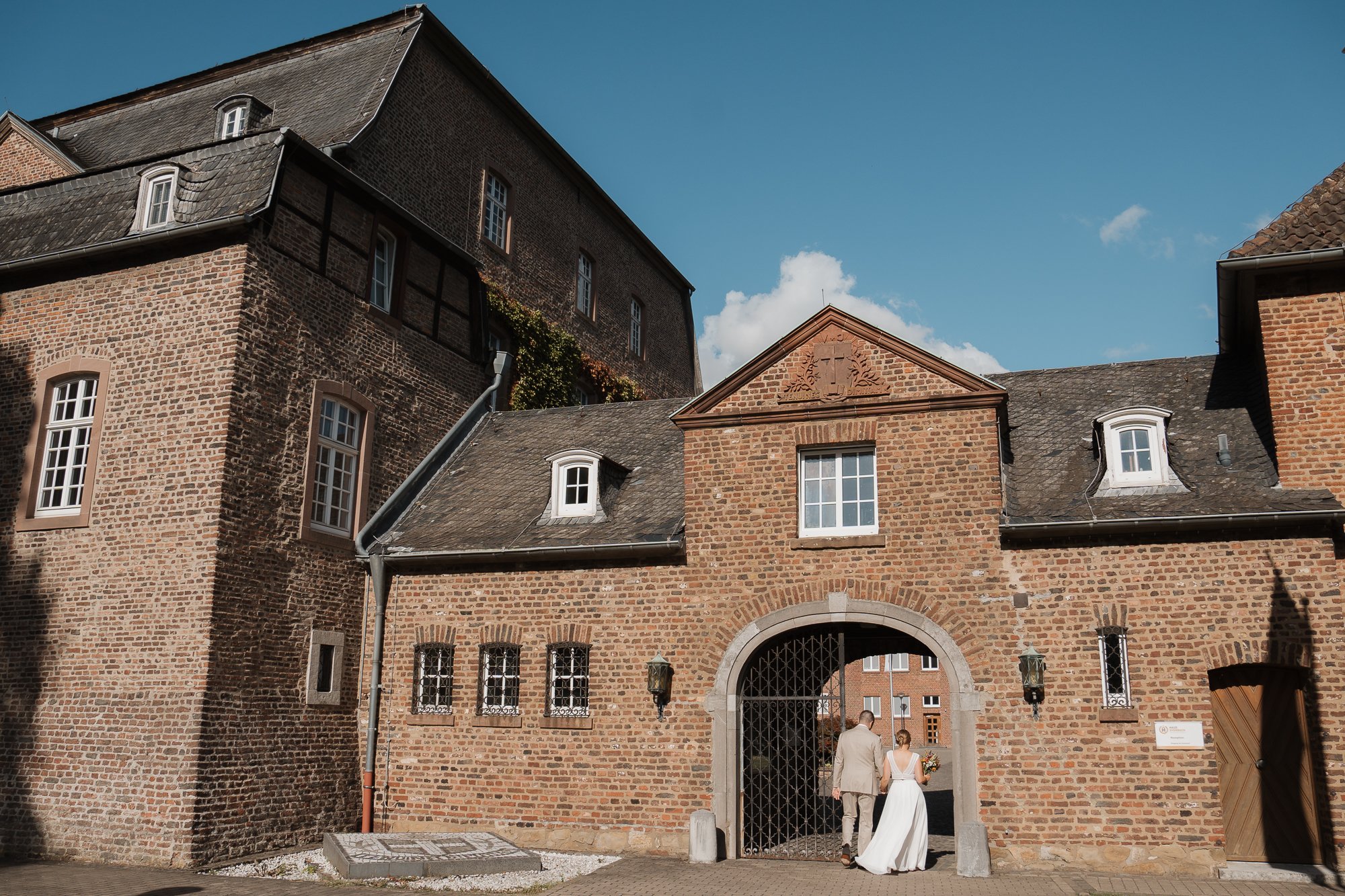 Ein Brautpaar verlässt ein altes, rotes Backsteingebäude bei Sonnenuntergang.