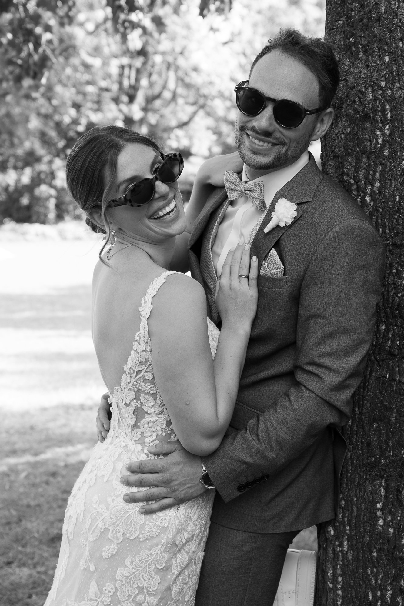 Ein lachendes Brautpaar mit Sonnenbrillen, bei ihrer Hochzeit im Freien, Schwarz-Weiß-Foto.
