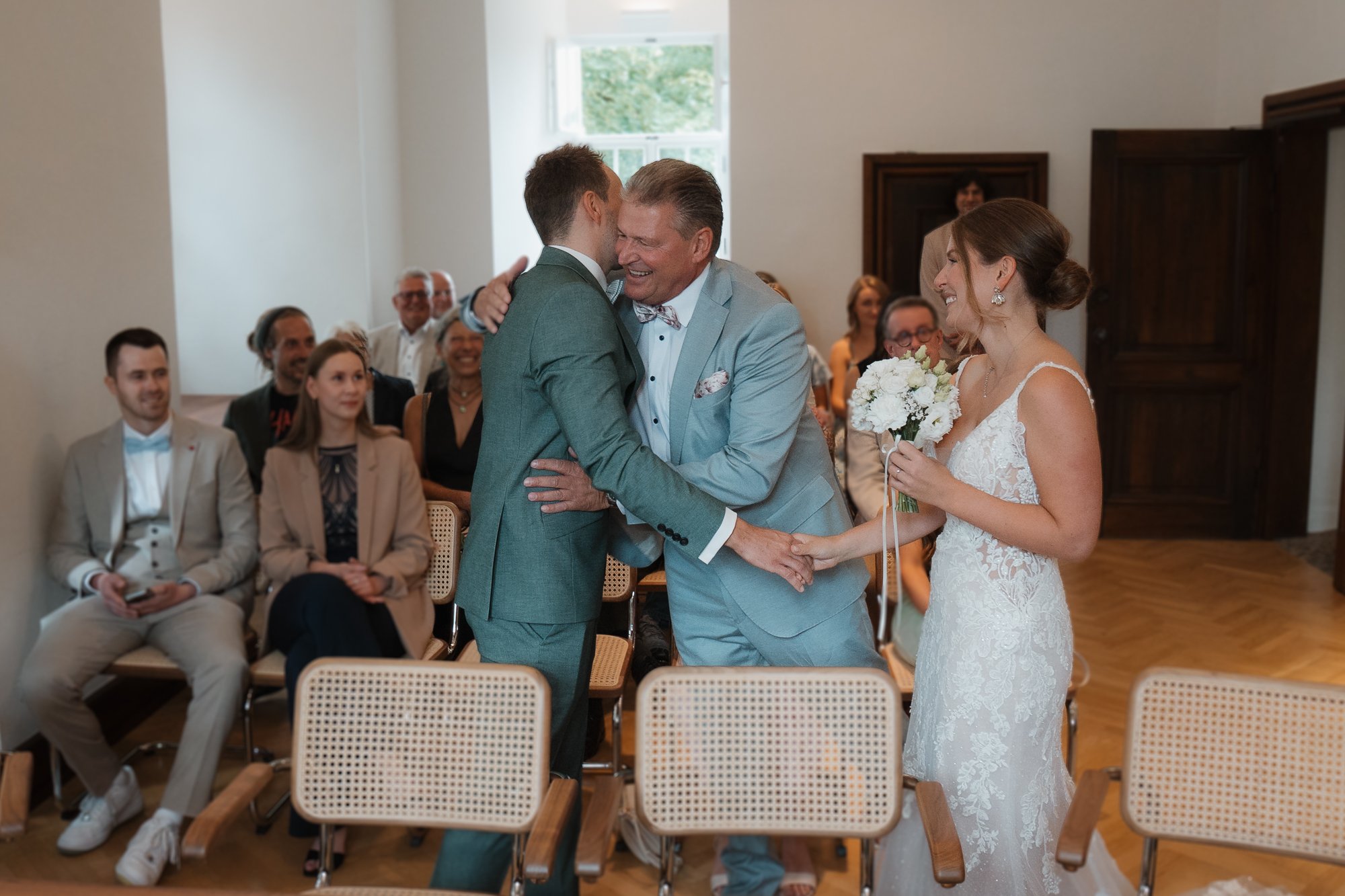 Ein Brautpaar bei ihrer Trauung, das sich die Hände hält, während der standesbeamte sie, umarmt.