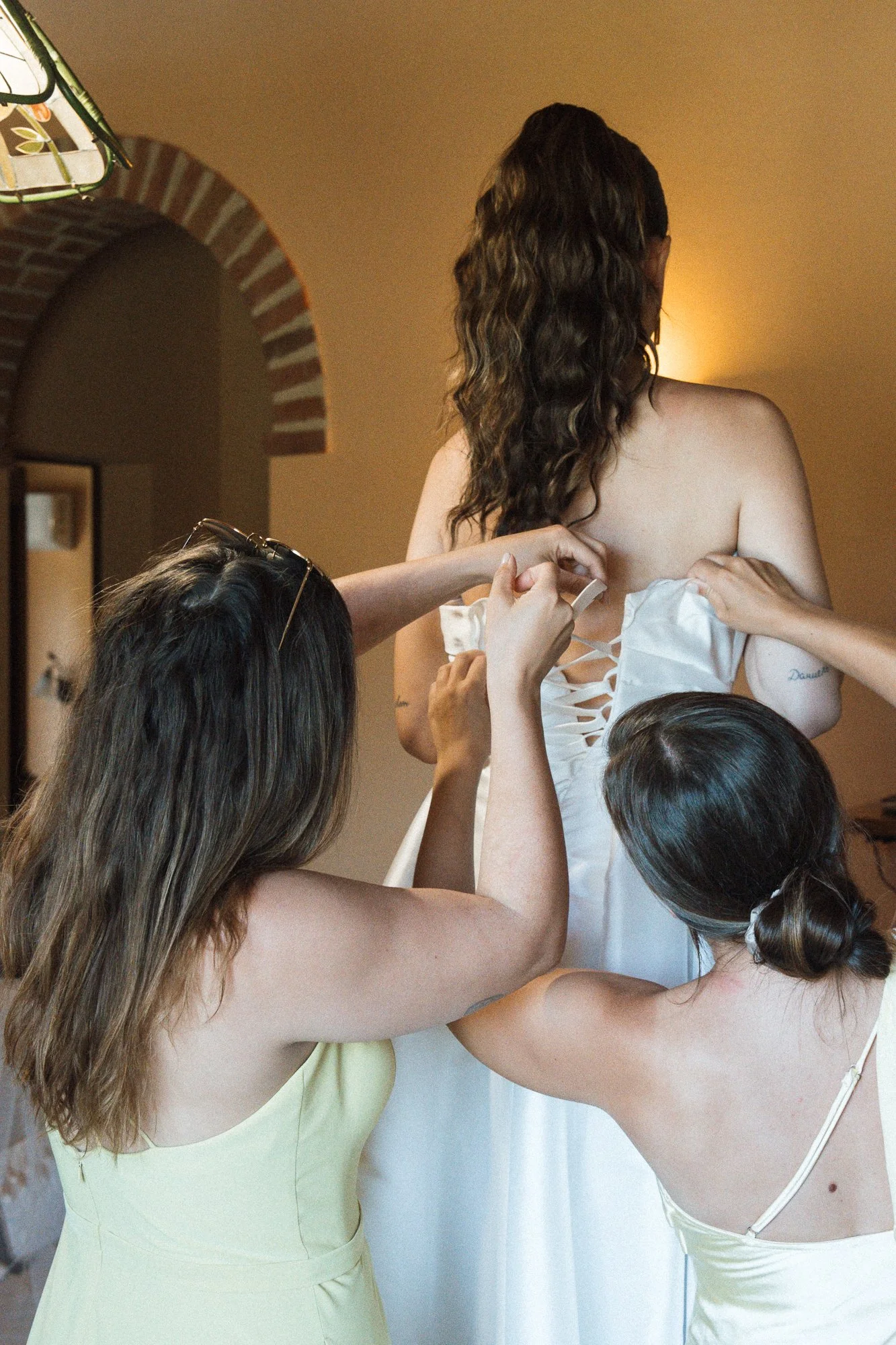 Drei Frauen helfen einer Braut, das weiße Hochzeitskleid anzuziehen.