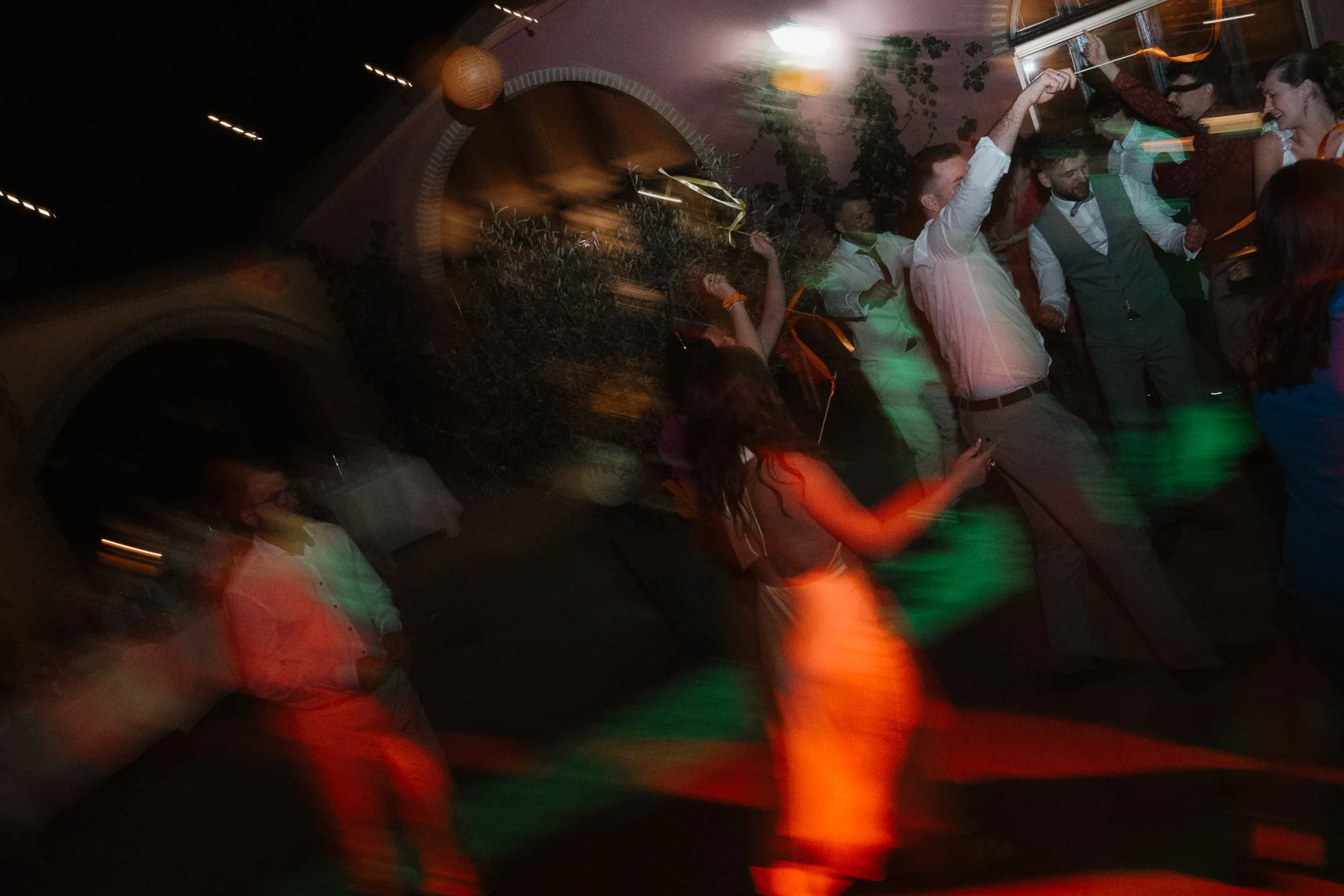 Menschen tanzen und feiern auf einer Party, mit bunten Lichtern und bewegten Bewegungen bei Nacht.