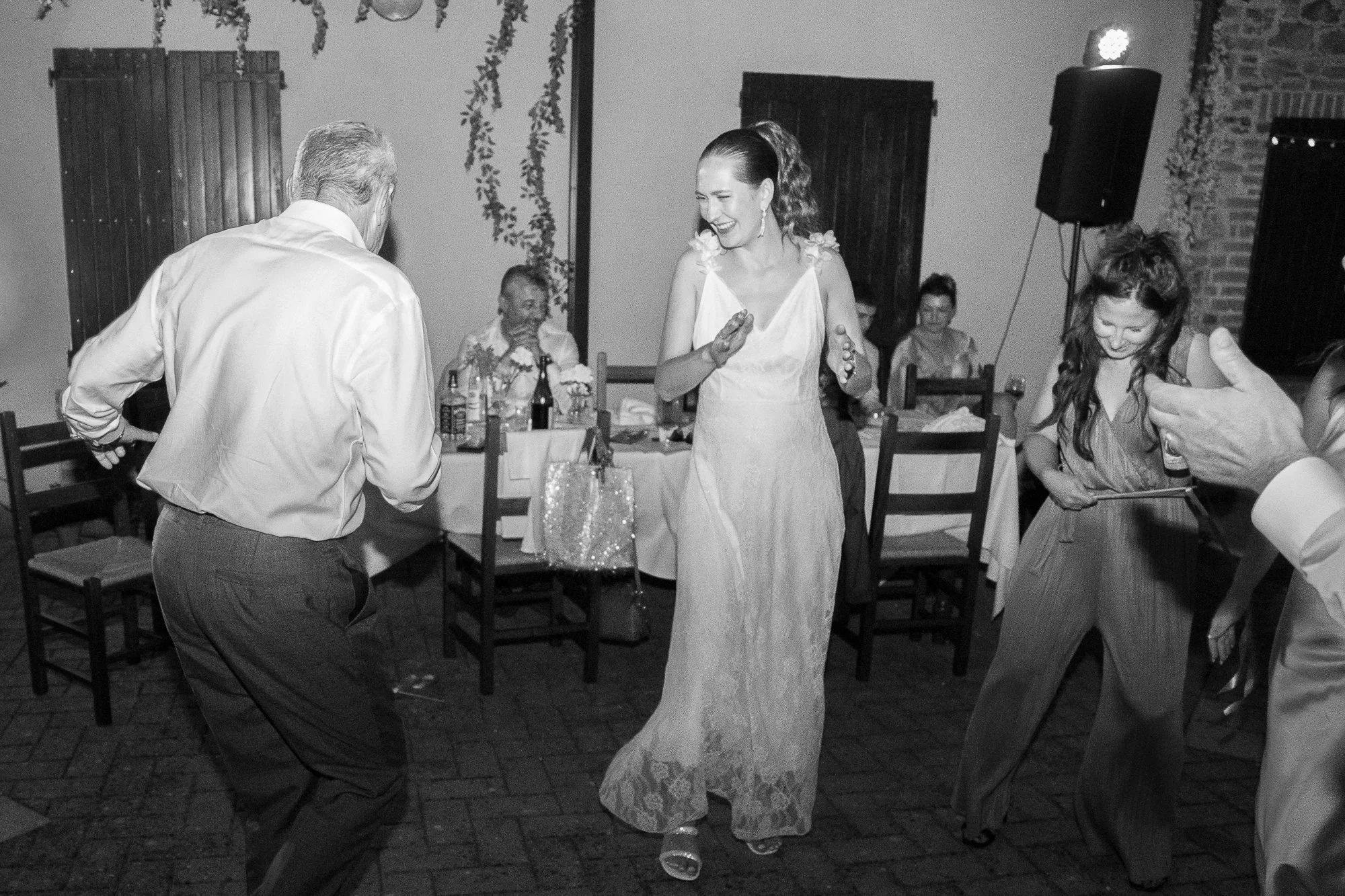 Menschen tanzen fröhlich auf einer Feier, eine Frau in einem weißen Kleid im Mittelpunkt, umgeben von anderen Gästen, die lachen und feiern.