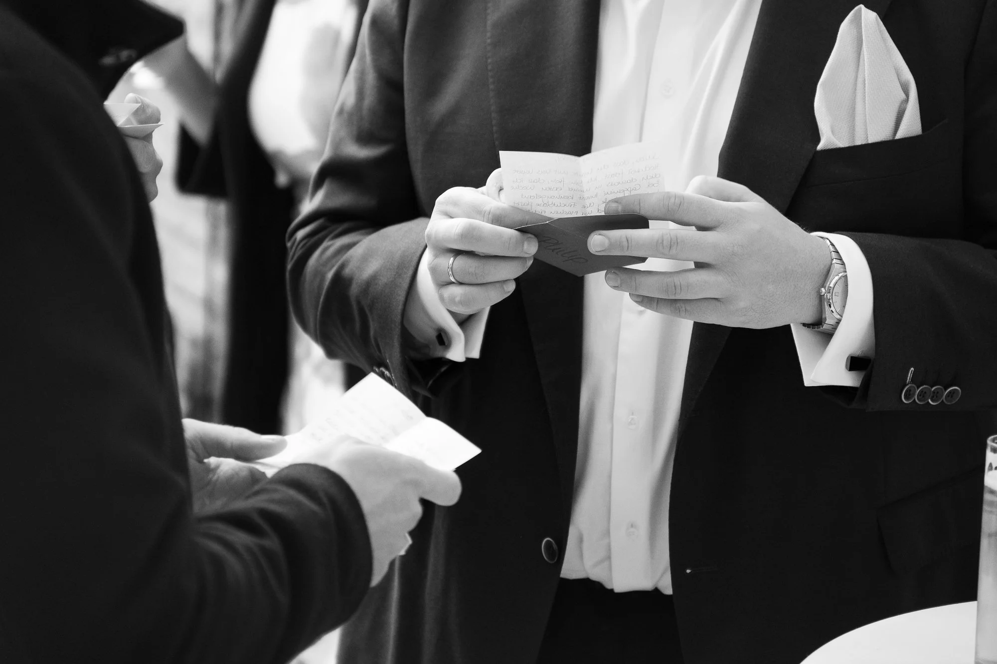 Zwei Männer in formeller Kleidung tauschen kleine Zettel aus, bei einem Event oder einer geschäftlichen Zusammenkunft.