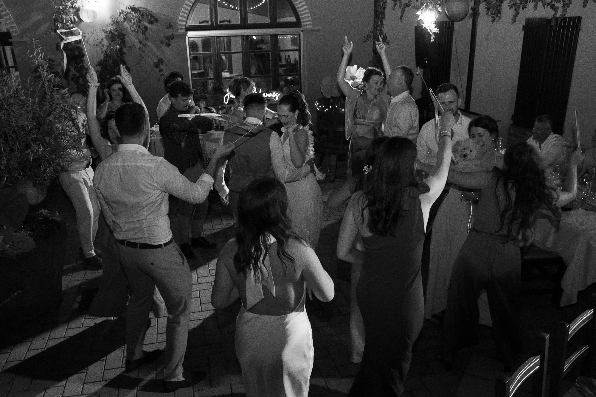 Menschen tanzen und feiern bei einer Party im Innenbereich, viele halten Kerzen, einige sitzen am Tisch, es gibt festliche Dekorationen und Lichter.