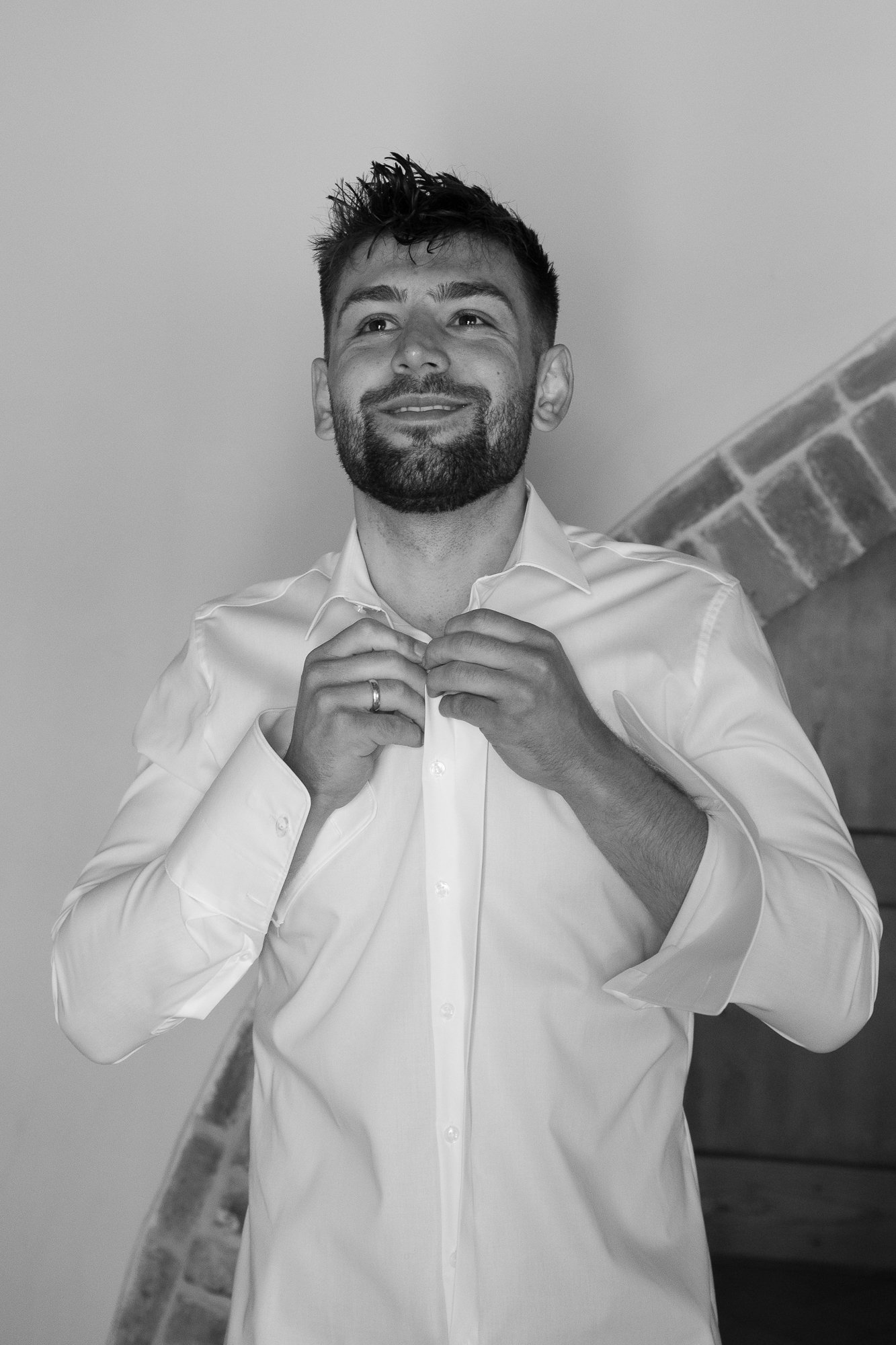 Ein Mann in einem weißen Hemd, der seine Knöpfe schließt, während er lächelt.